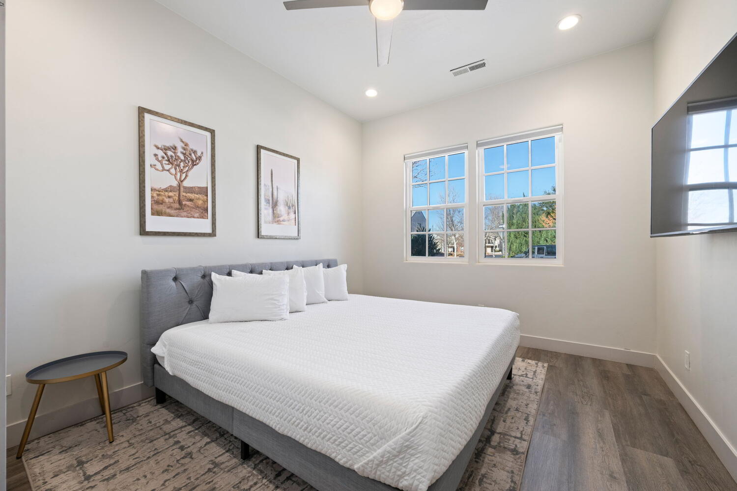 Room featuring wood-finish flooring, two large windows, a ceiling fan with integrated lighting, recessed lighting, and a wall-mounted television