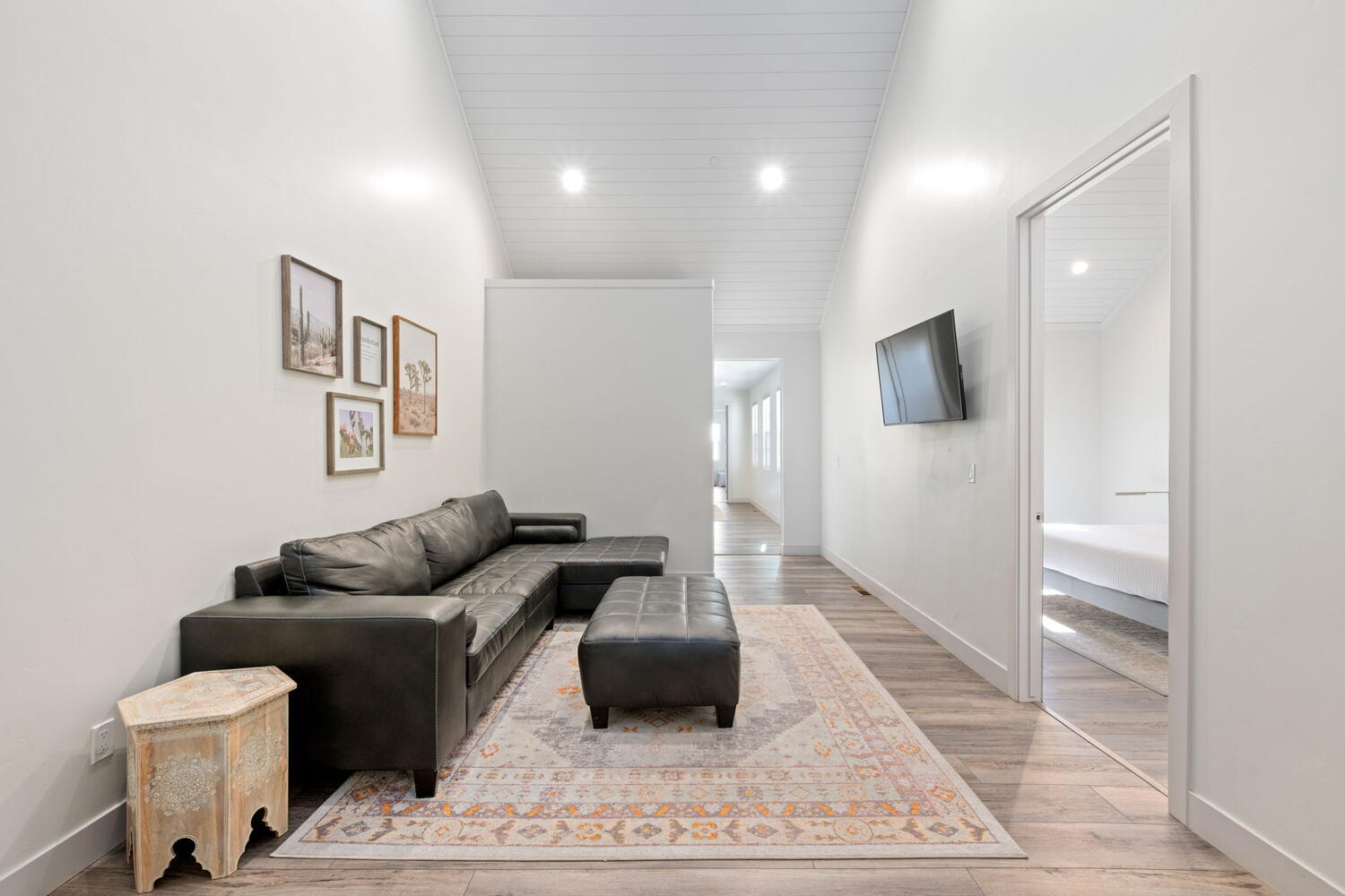 Spacious area featuring wood-finish flooring, white walls, and a vaulted ceiling with recessed lighting