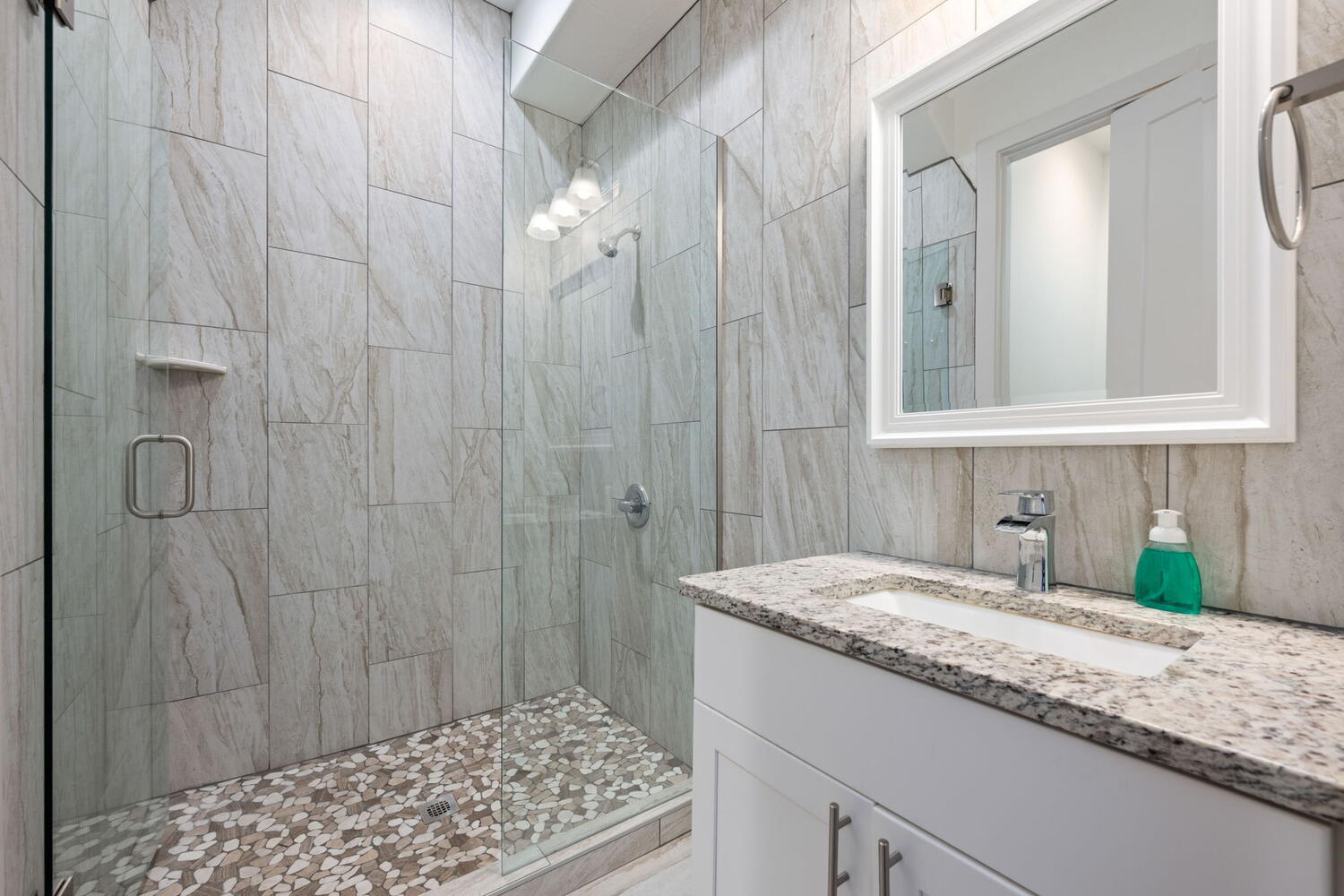 Contemporary bathroom featuring a frameless glass shower enclosure with pebble floor tiles and large format wall tiles