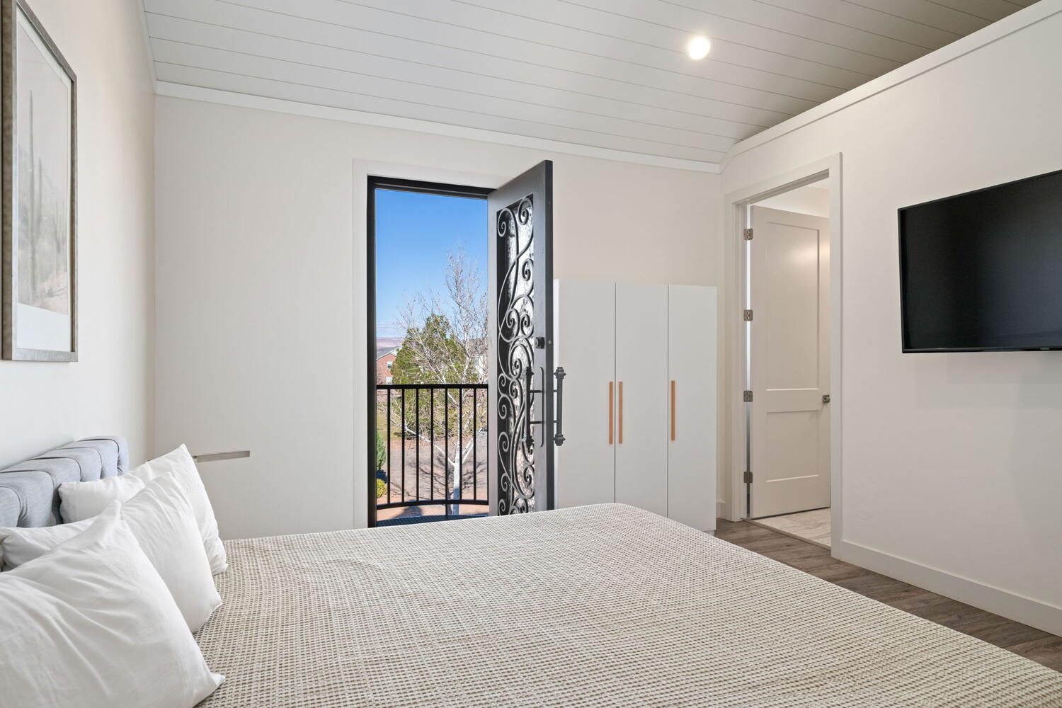 Bedroom featuring a decorative wrought-iron balcony door, vaulted shiplap ceiling, and light wood-finish flooring