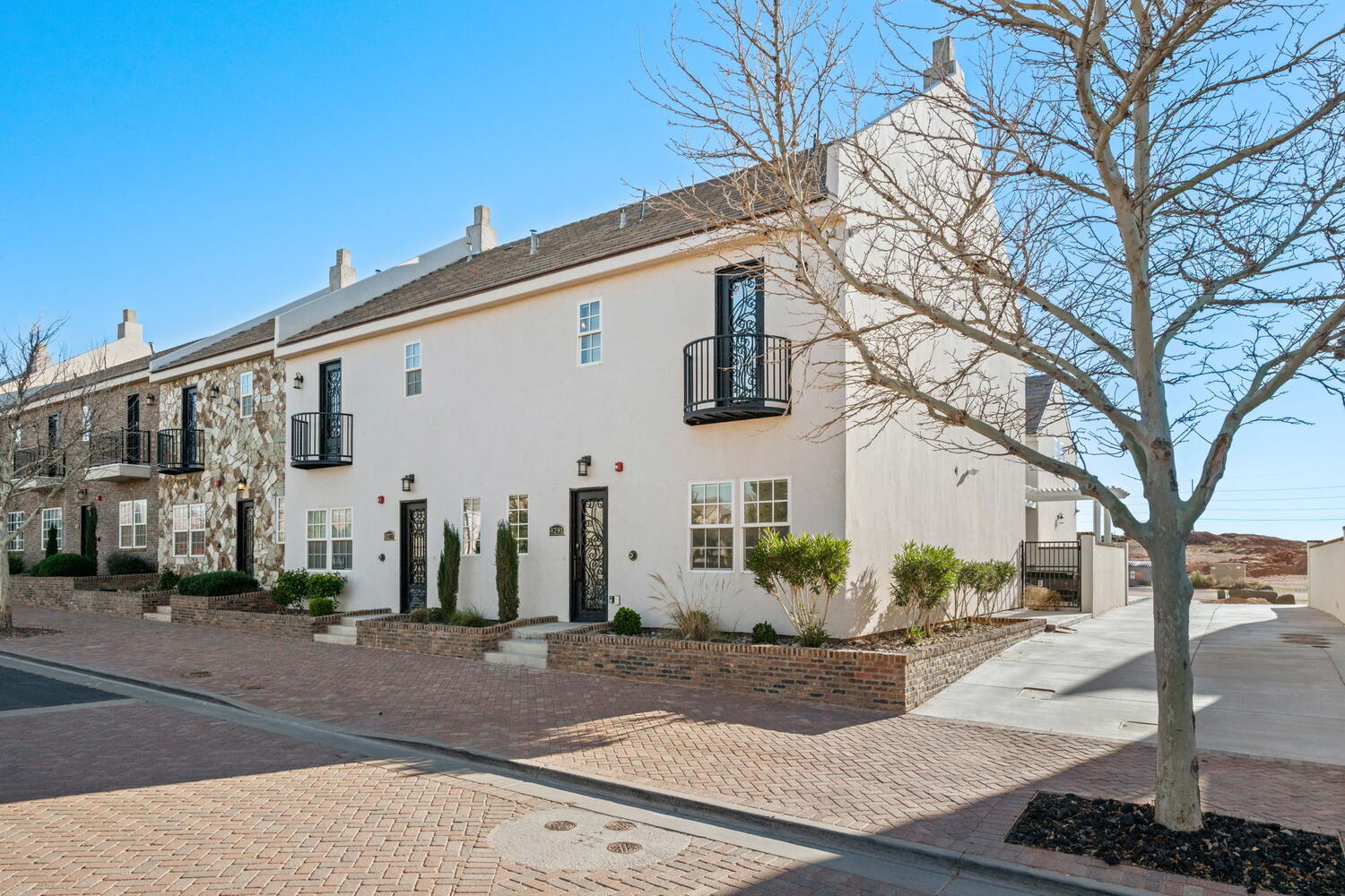 Two-story stucco townhouse with a dark tile roof, a black wrought iron balcony, and dark-framed windows