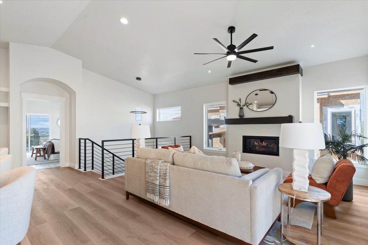 Spacious living area featuring light wood-finish flooring, a contemporary fireplace, and a striking black ceiling fan