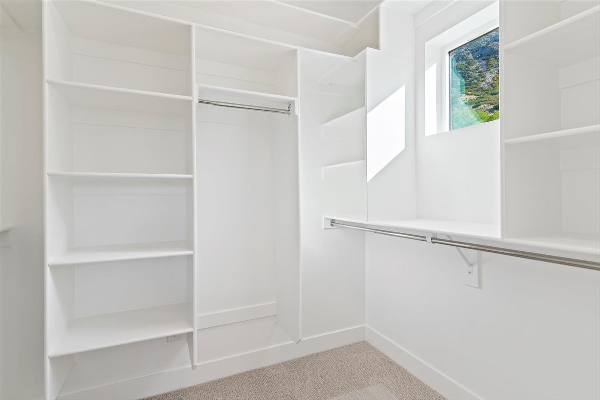 Walk-in closet featuring white built-in shelving, hanging rods, and a window