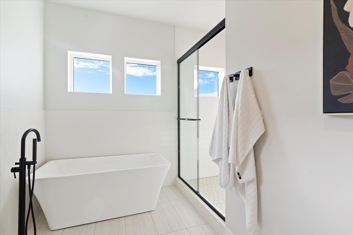 Freestanding tub with matte black floor-mounted faucet, complemented by a glass-enclosed shower with black trim and a tiled floor