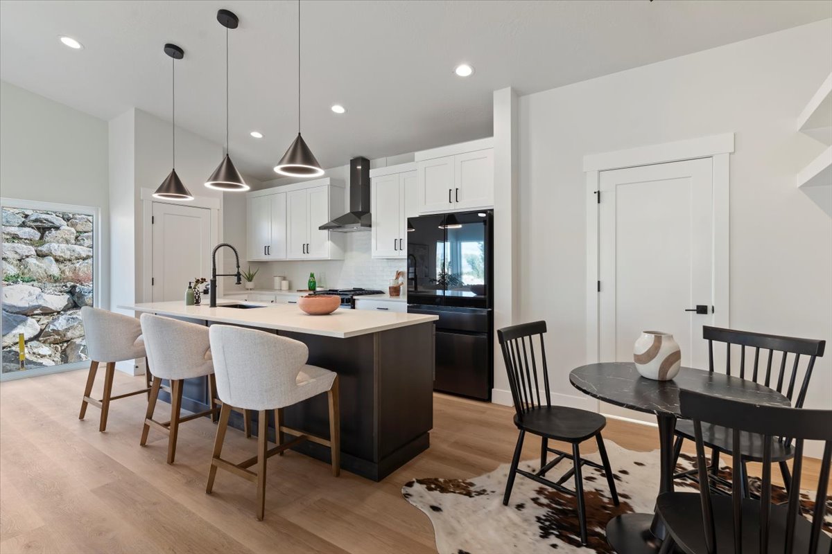 Modern kitchen featuring a large central island with seating, white shaker cabinetry, black stainless steel appliances, and wood-finish flooring