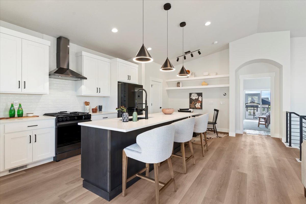 Modern kitchen featuring a dark-toned island with white countertop, white cabinetry with dark hardware, a stainless steel range hood, and wood-finish flooring