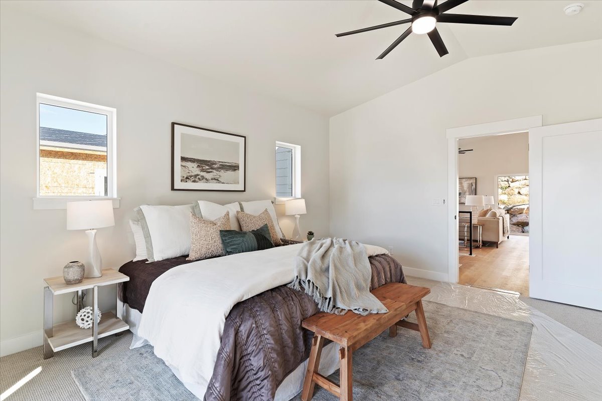 Vaulted ceiling bedroom featuring light neutral wall tones, a modern ceiling fan with integrated lighting, and dual windows