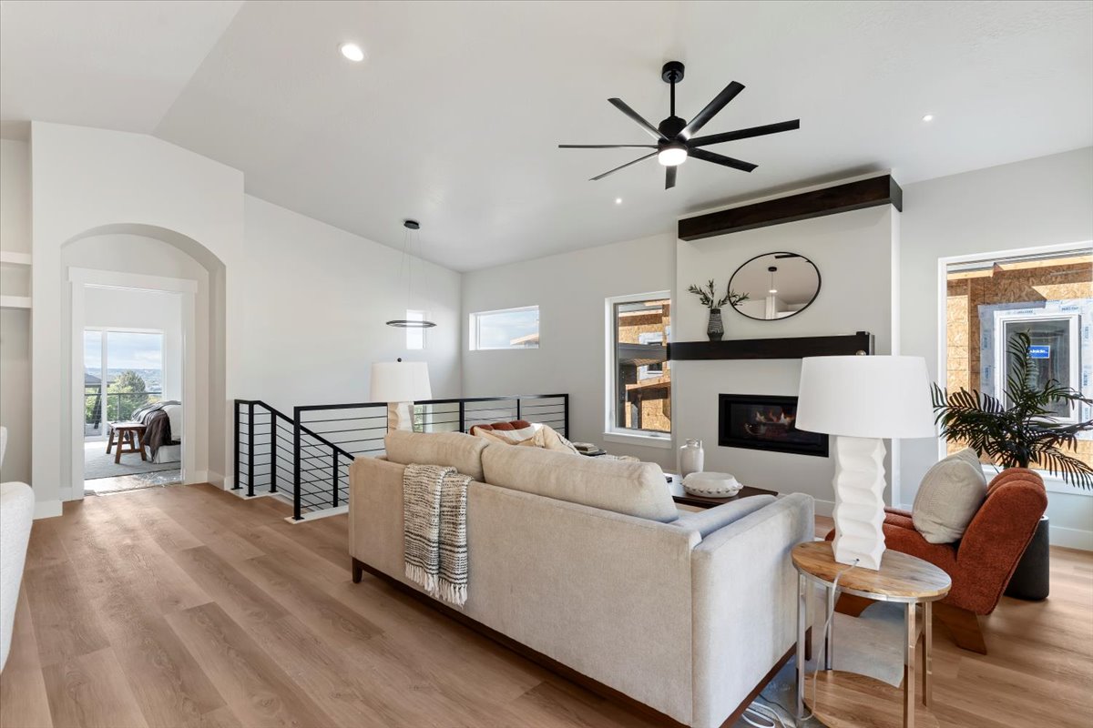 Living area featuring wood-finish flooring, a contemporary ceiling fan, and a fireplace with a dark wood mantle