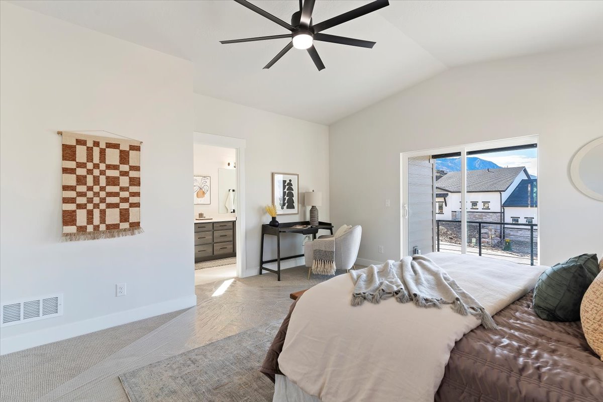 Vaulted ceiling with a contemporary ceiling fan, sliding glass door leading to an outdoor balcony, mountain backdrop, and an en-suite bathroom featuring a double vanity with grey cabinetry and an undermount sink