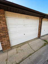 White paneled automatic  garage door with an overhead brown gutter system, textured stucco facade, and brick pillar detailing