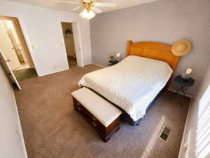 Carpeted room featuring a ceiling fan with integrated lighting, textured wall finish, and an entryway to another room with a visible white toilet and vanity