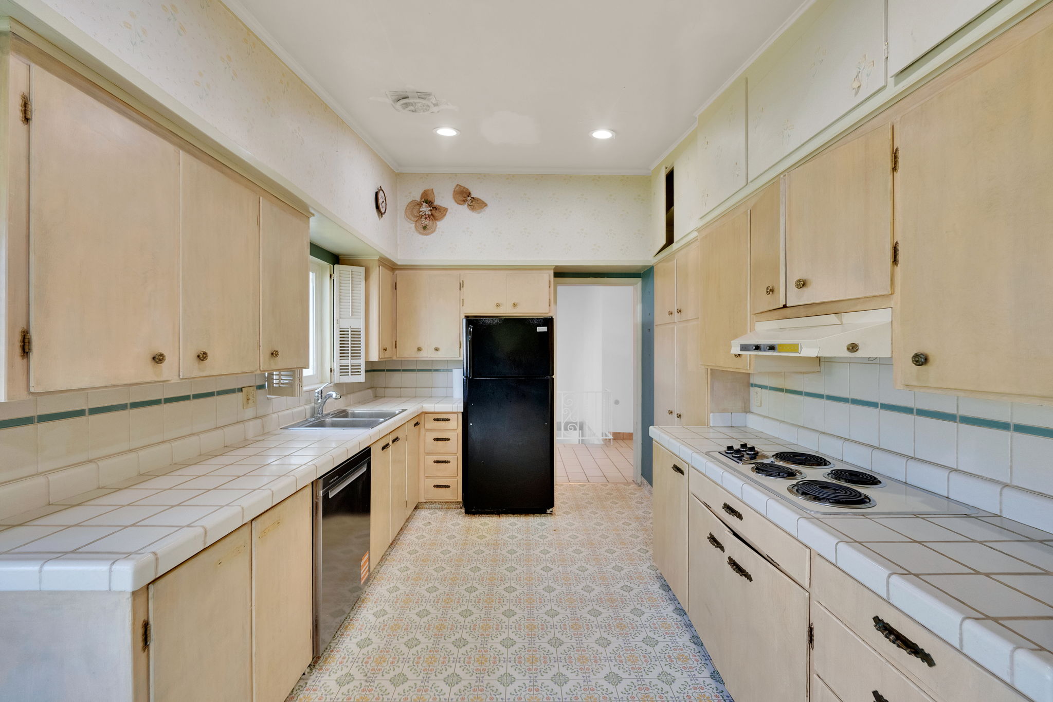 Galley kitchen featuring extensive upper and lower cabinetry, white tile countertops, and patterned floor tile