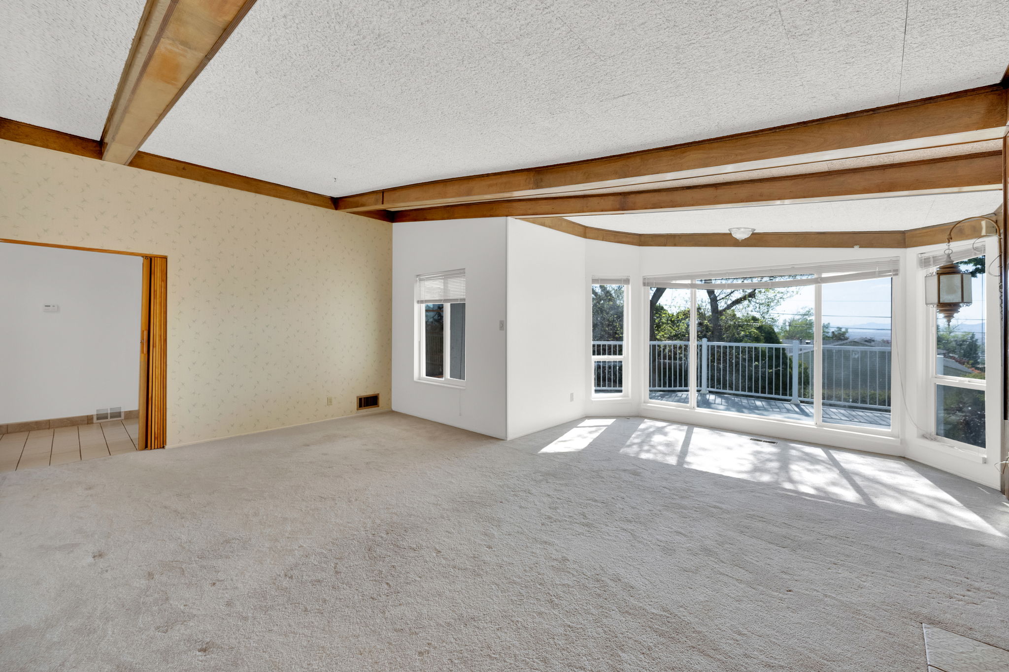Spacious room featuring exposed wood beams, expansive floor-to-ceiling windows, and light-colored carpeting
