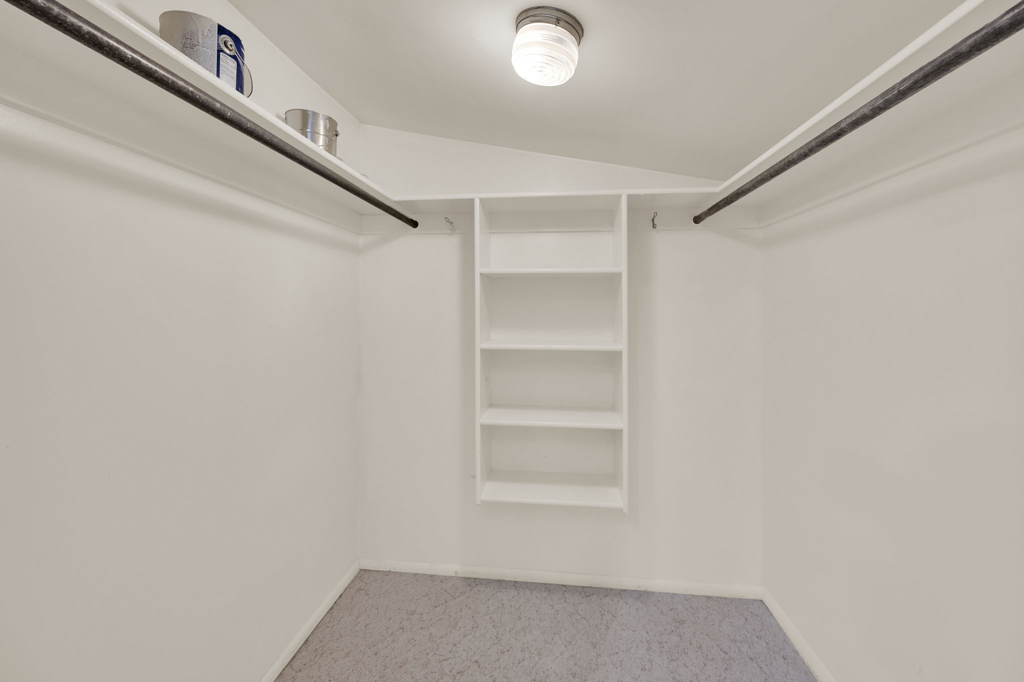 Walk-in closet with built-in shelving, dual hanging rods, upper storage shelves, and overhead lighting
