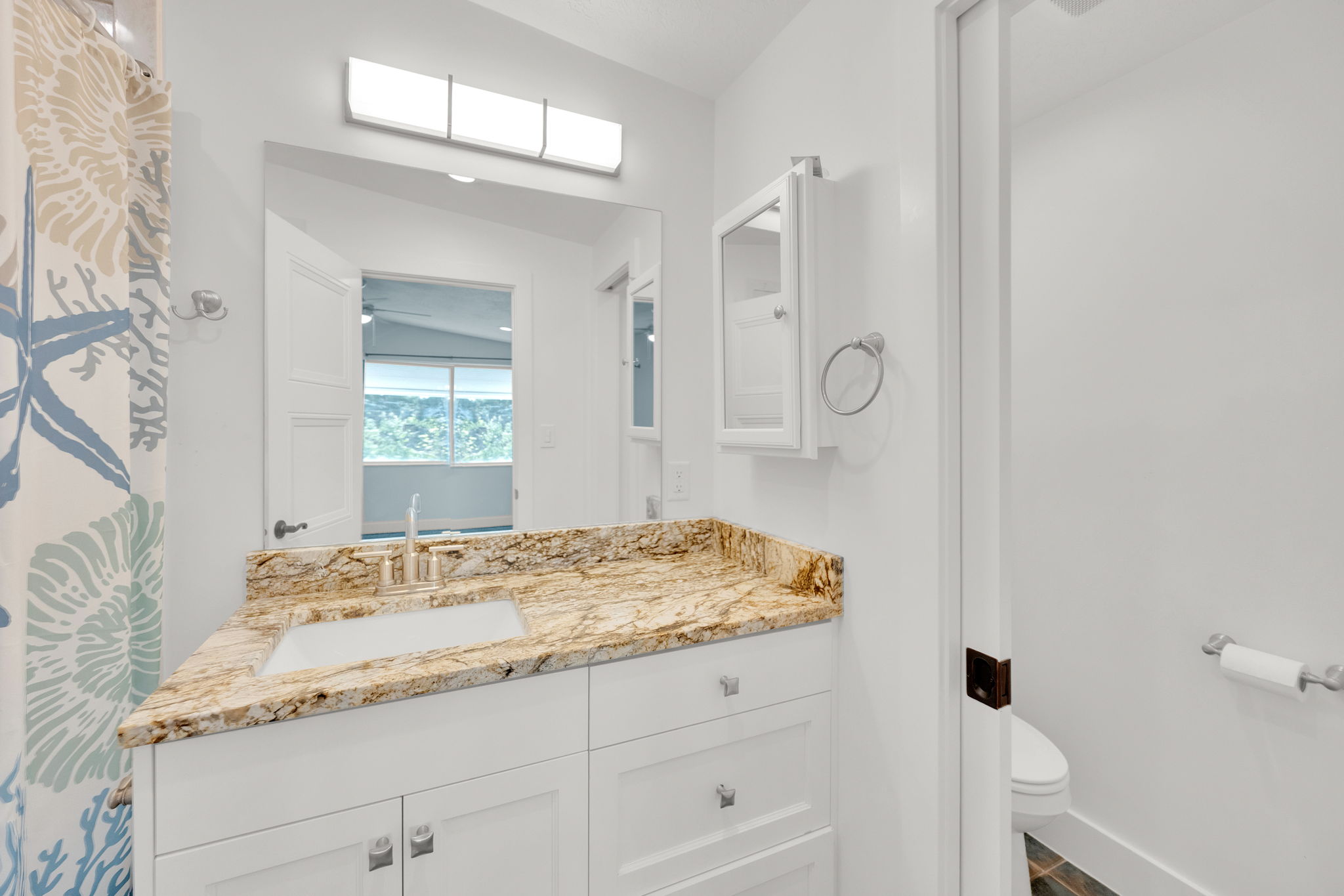 Bathroom vanity with a rectangular undermount sink, a polished chrome faucet, and a light-toned patterned countertop