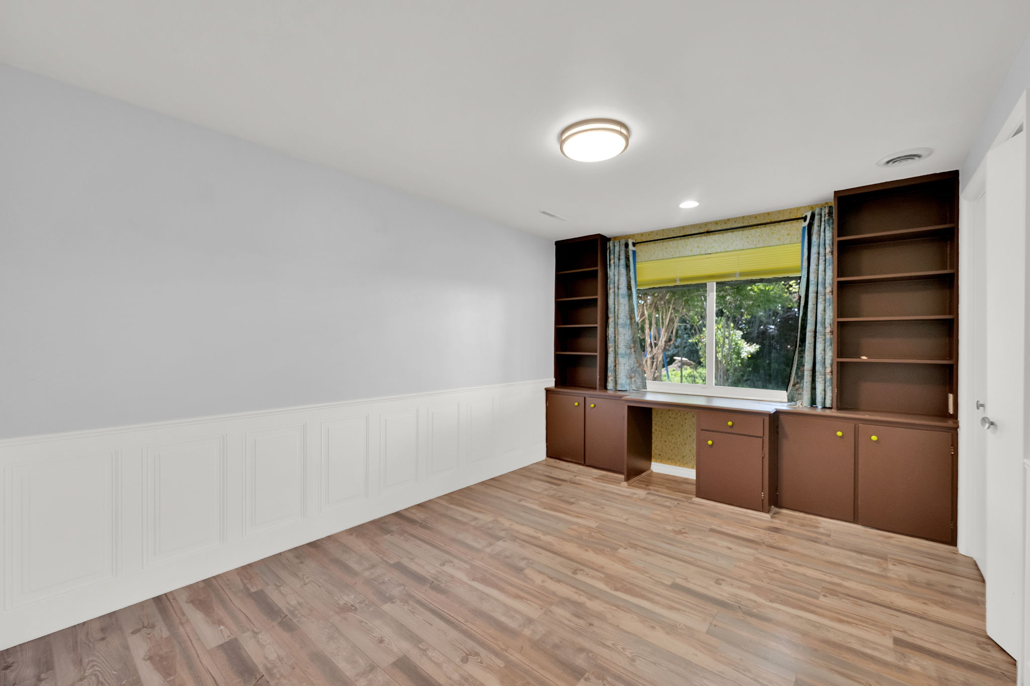 Room featuring wood-finish flooring, wainscoting, and a window with a green outdoor backdrop