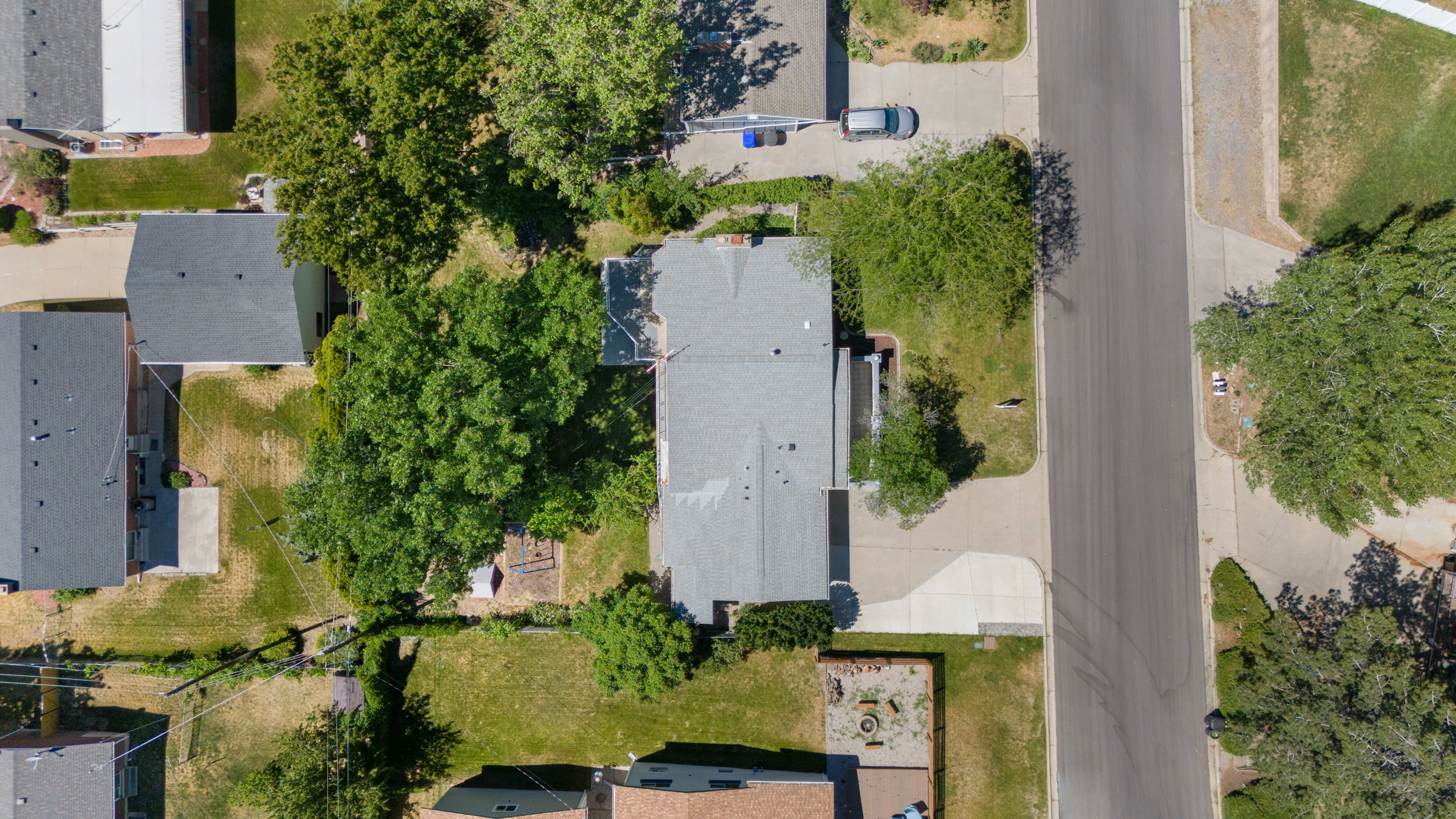 Property featuring a gray shingle roof, mature trees, a paved driveway, and a concrete patio