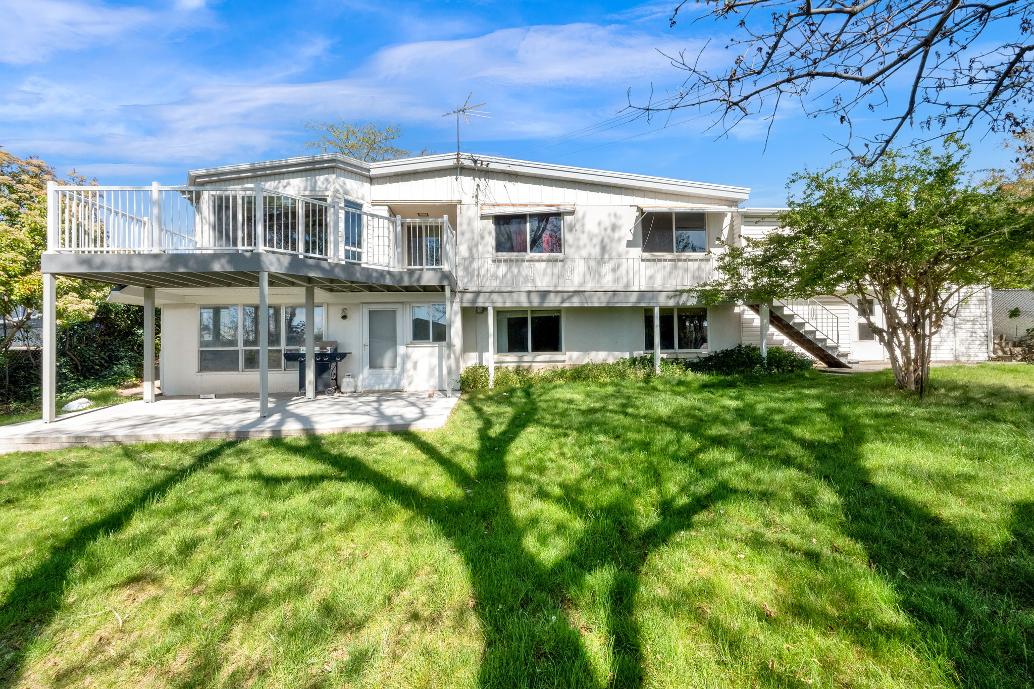 Multi-level residence featuring a large upper-level deck with white railings, a lower-level patio, and a spacious green lawn