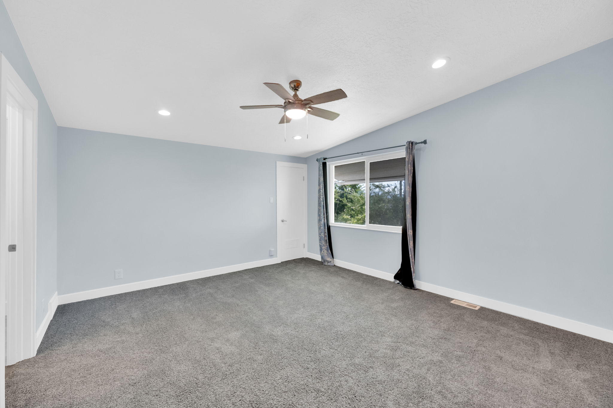 Spacious room featuring light blue walls, gray carpet, and a white trim baseboard