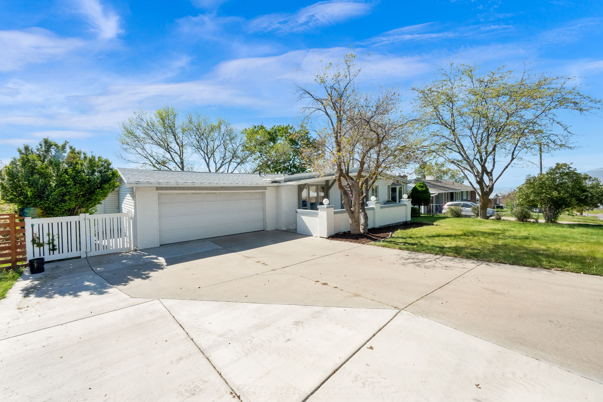 Exterior of a single-story residence featuring a two-car garage, white siding, and a white picket fence