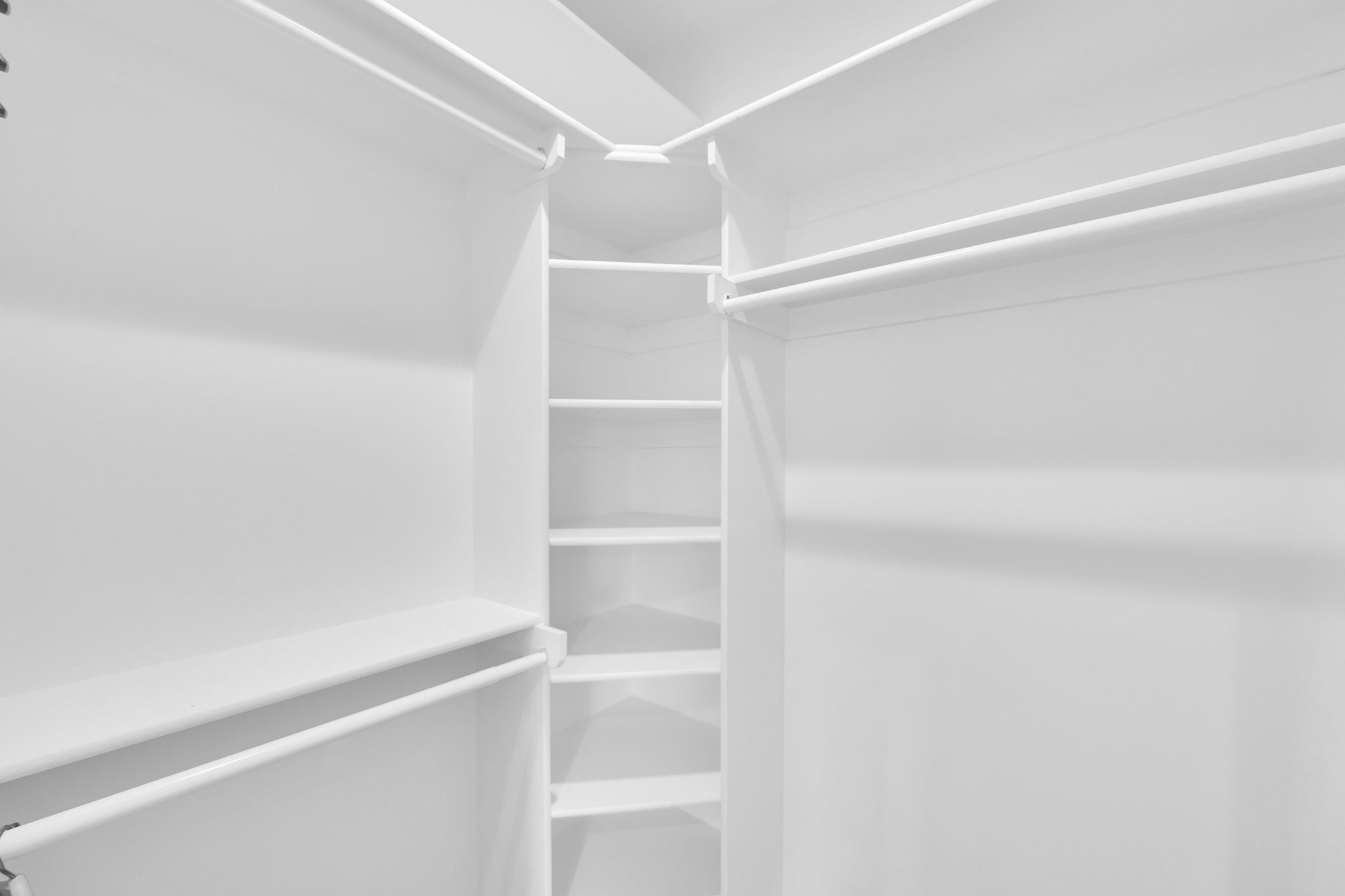 Spacious walk-in closet featuring white built-in shelving, multiple hanging rods, and ample storage capacity