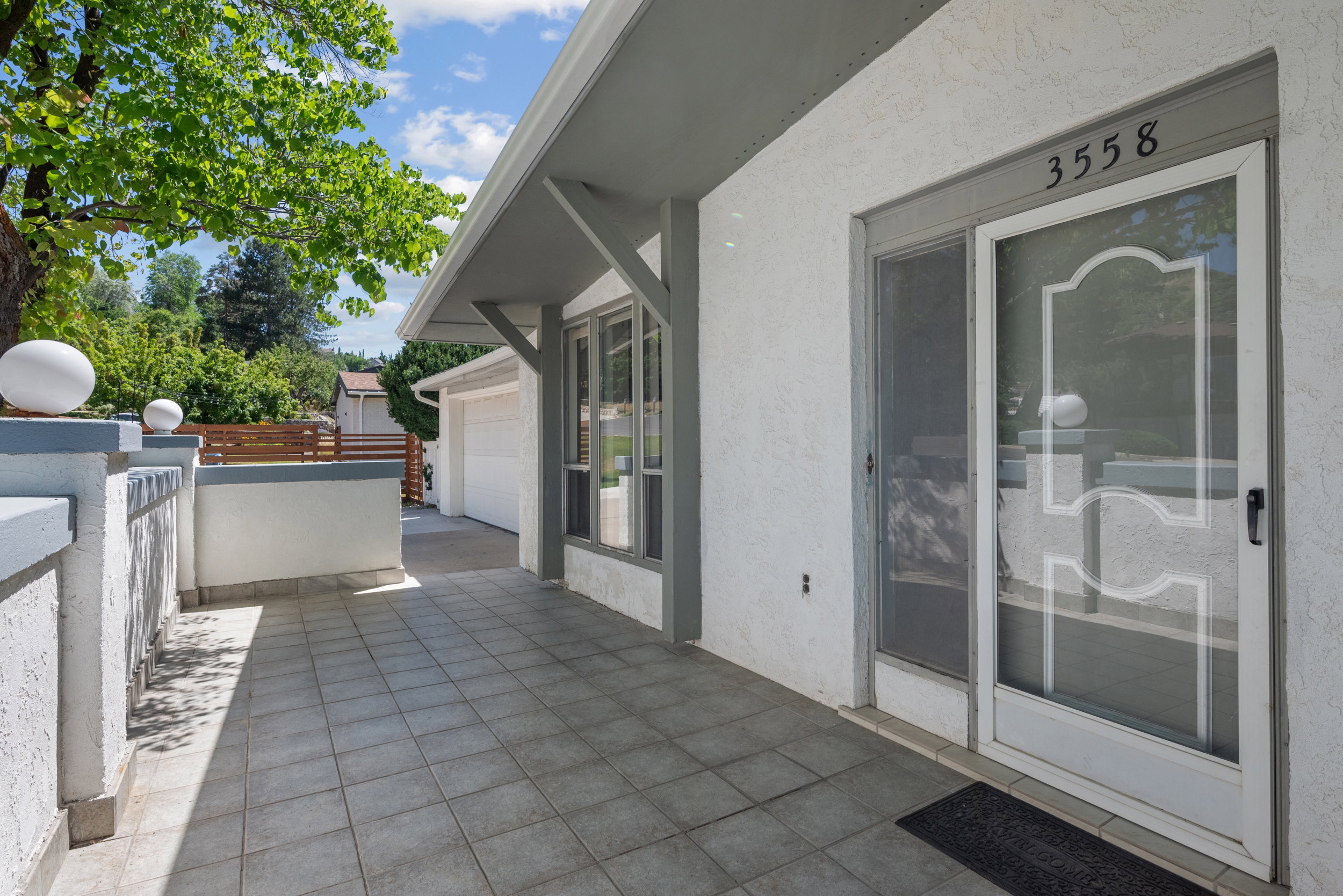 Tiled entry porch featuring white stucco exterior, grey trim accents, and an attached awning