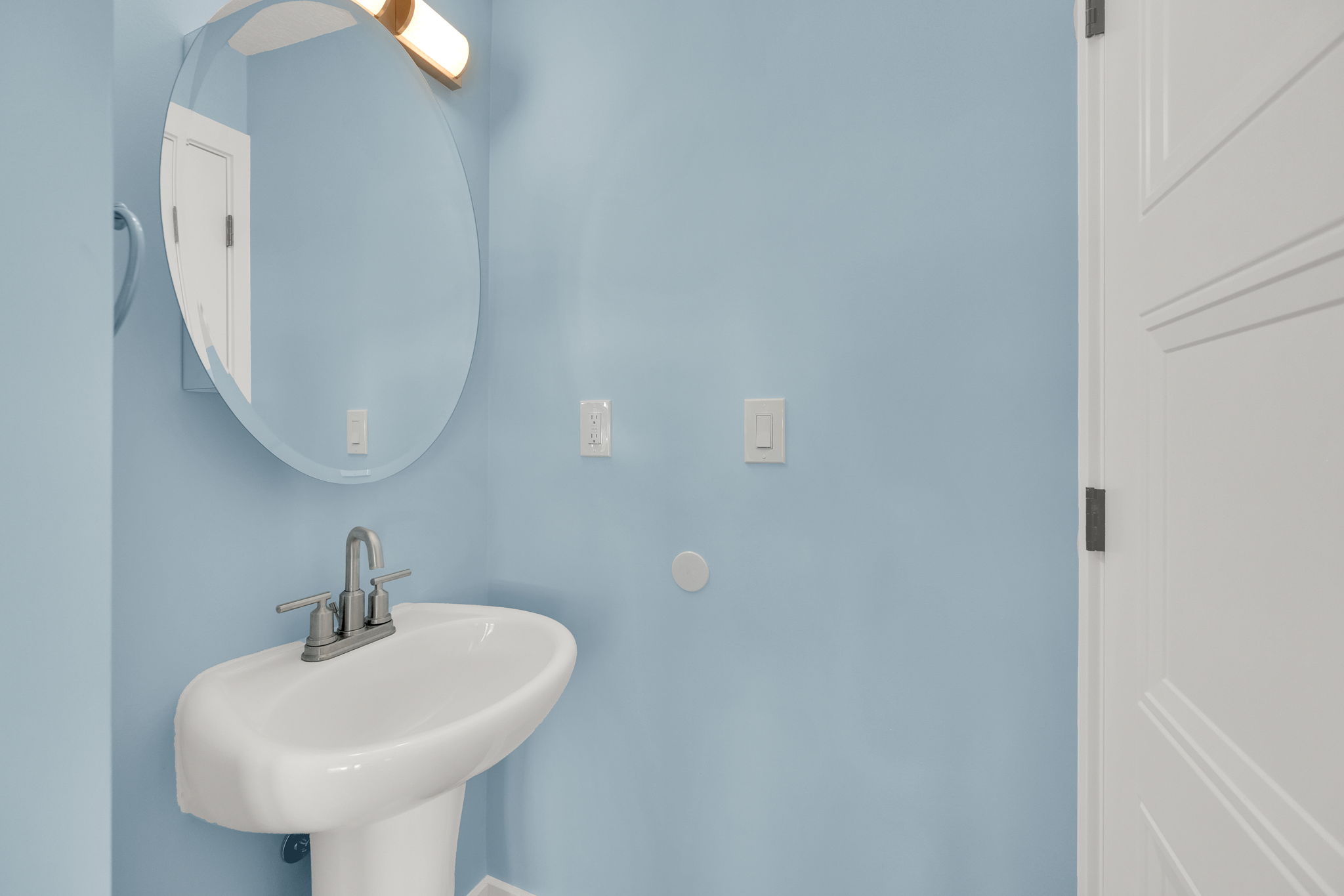 Pedestal sink with a two-handle faucet, oval mirror, and contemporary vanity lighting