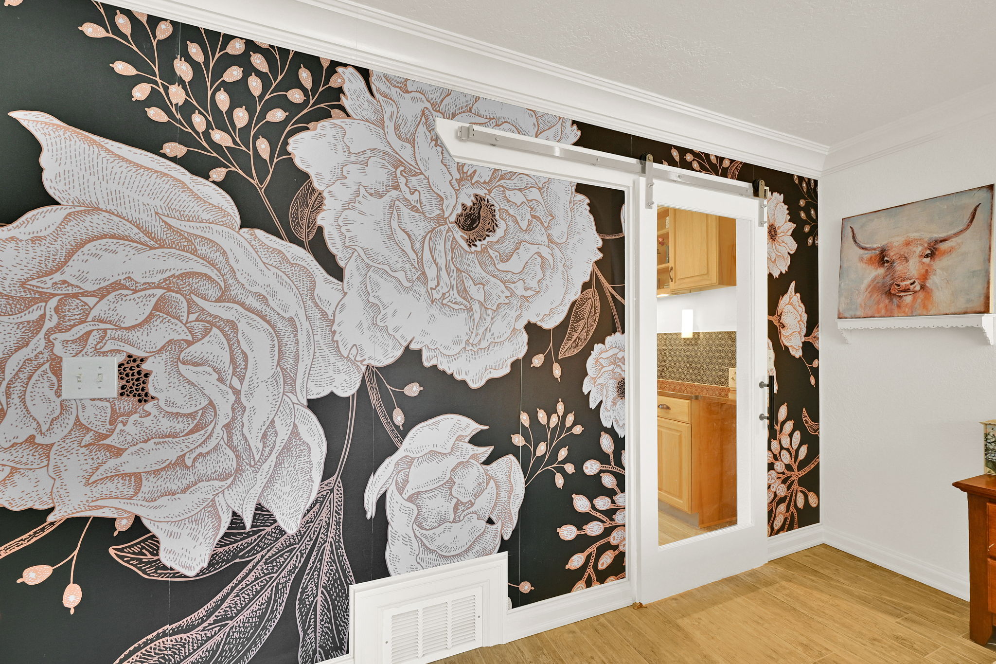 Feature wall with large-scale floral pattern wallpaper, white crown molding, and wood-finish flooring