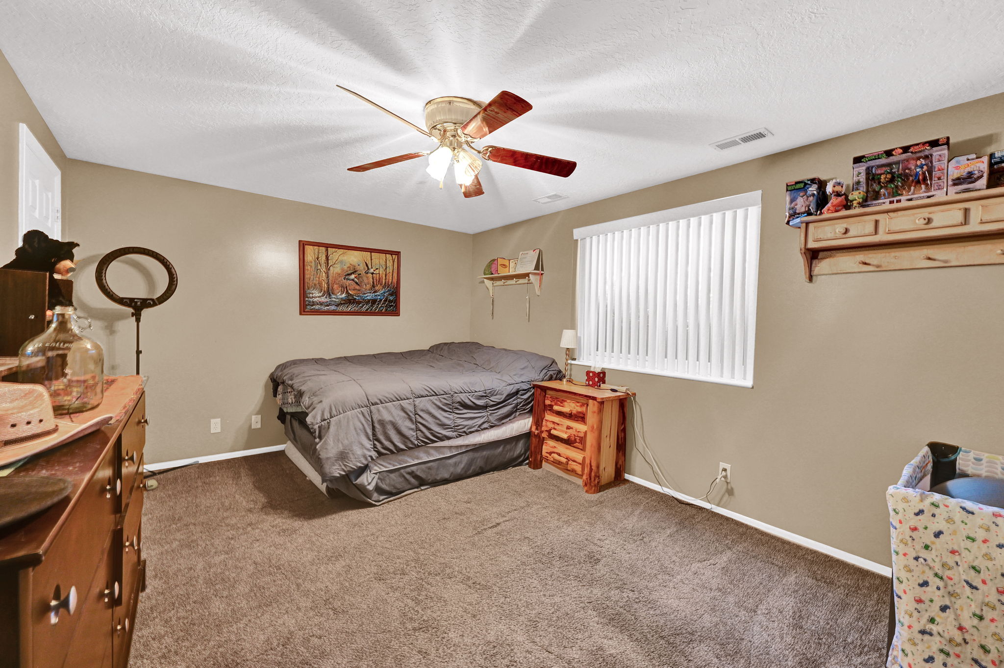 Carpeted interior room featuring neutral wall paint, a ceiling fan with integrated lighting, and a window with vertical blinds