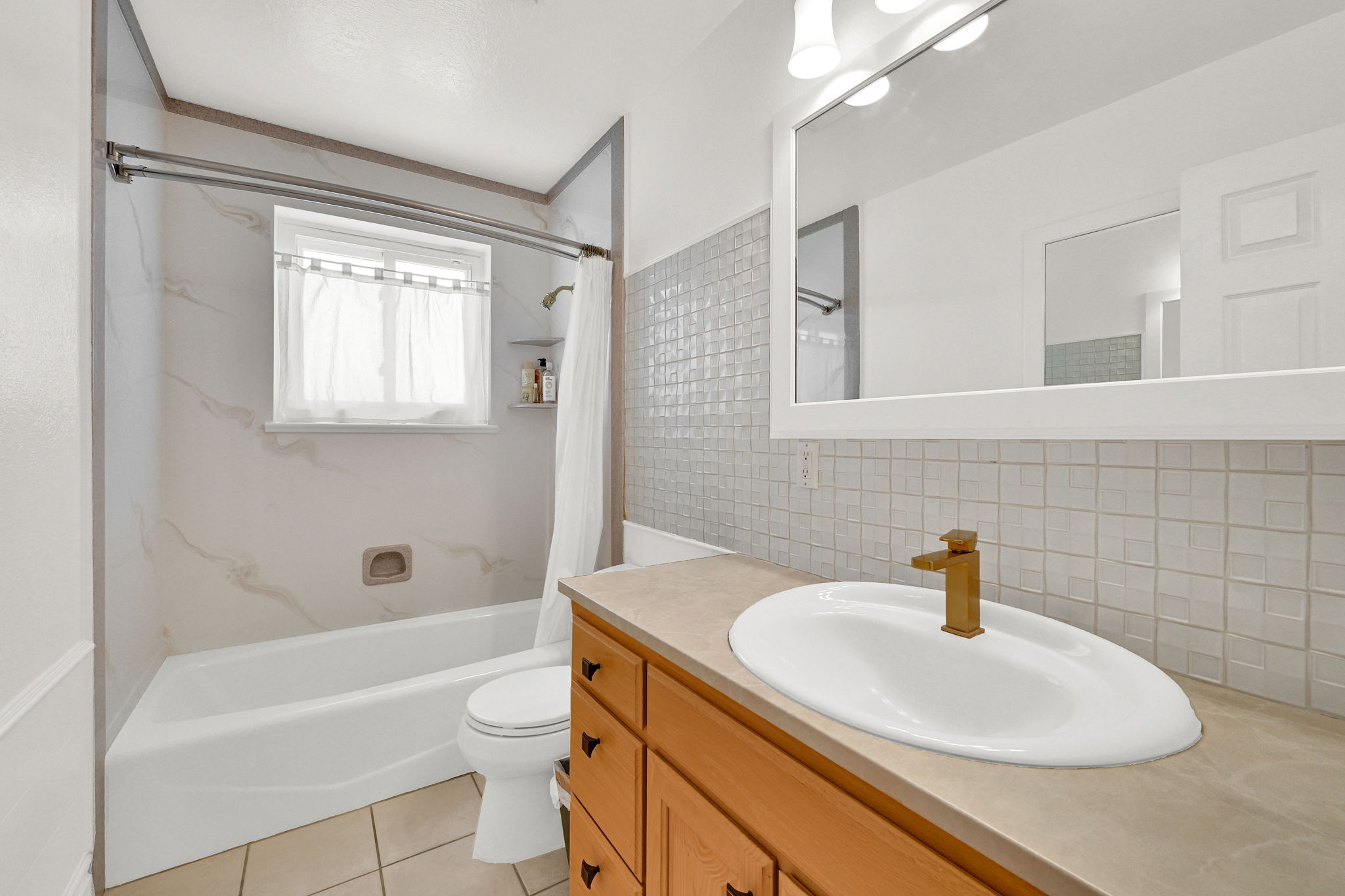 Bathroom featuring a single vanity with a golden-hued faucet, a framed mirror, and light wood cabinetry