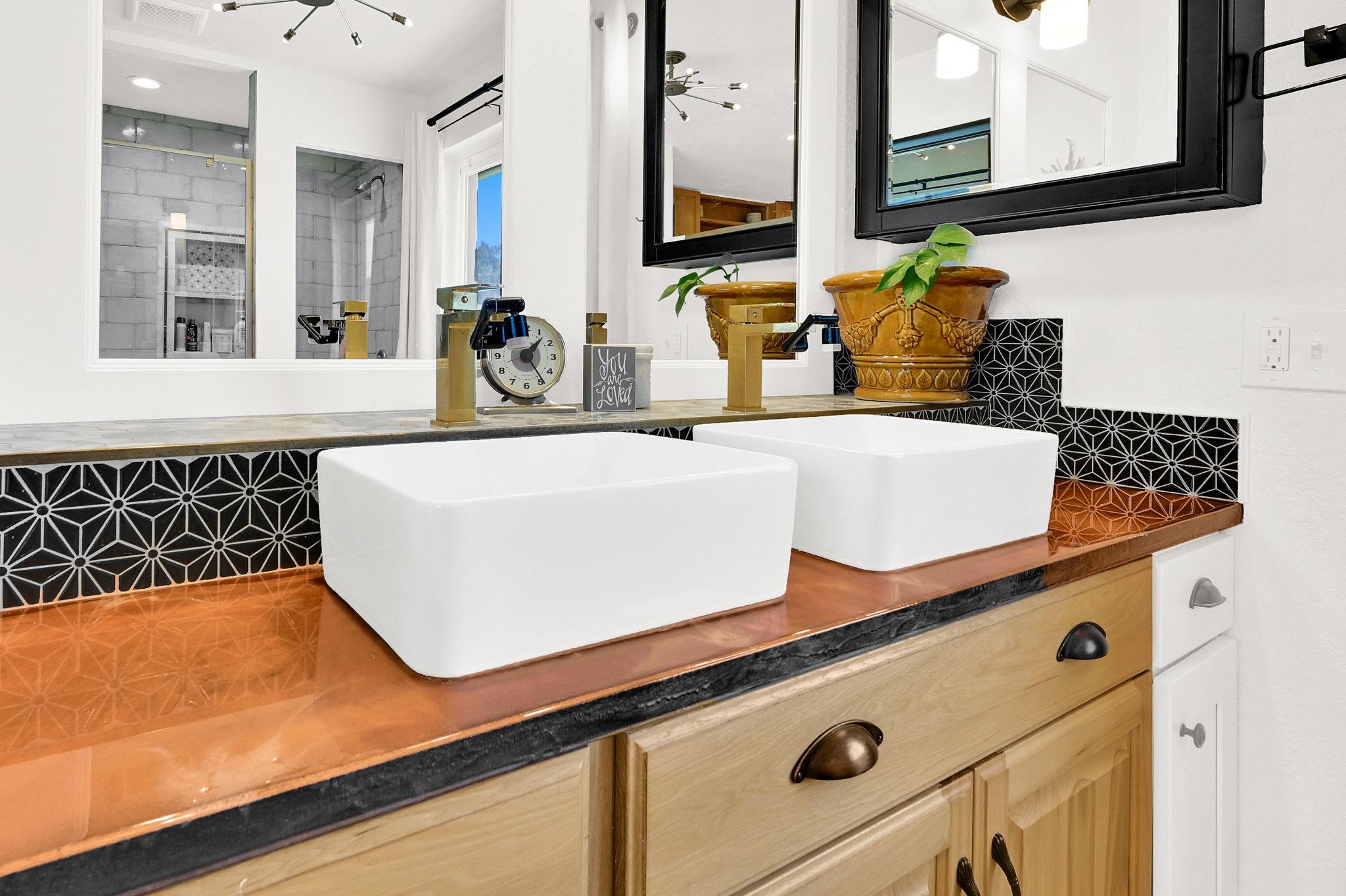 Dual vessel sinks set atop a copper-finish countertop with a geometric tile backsplash