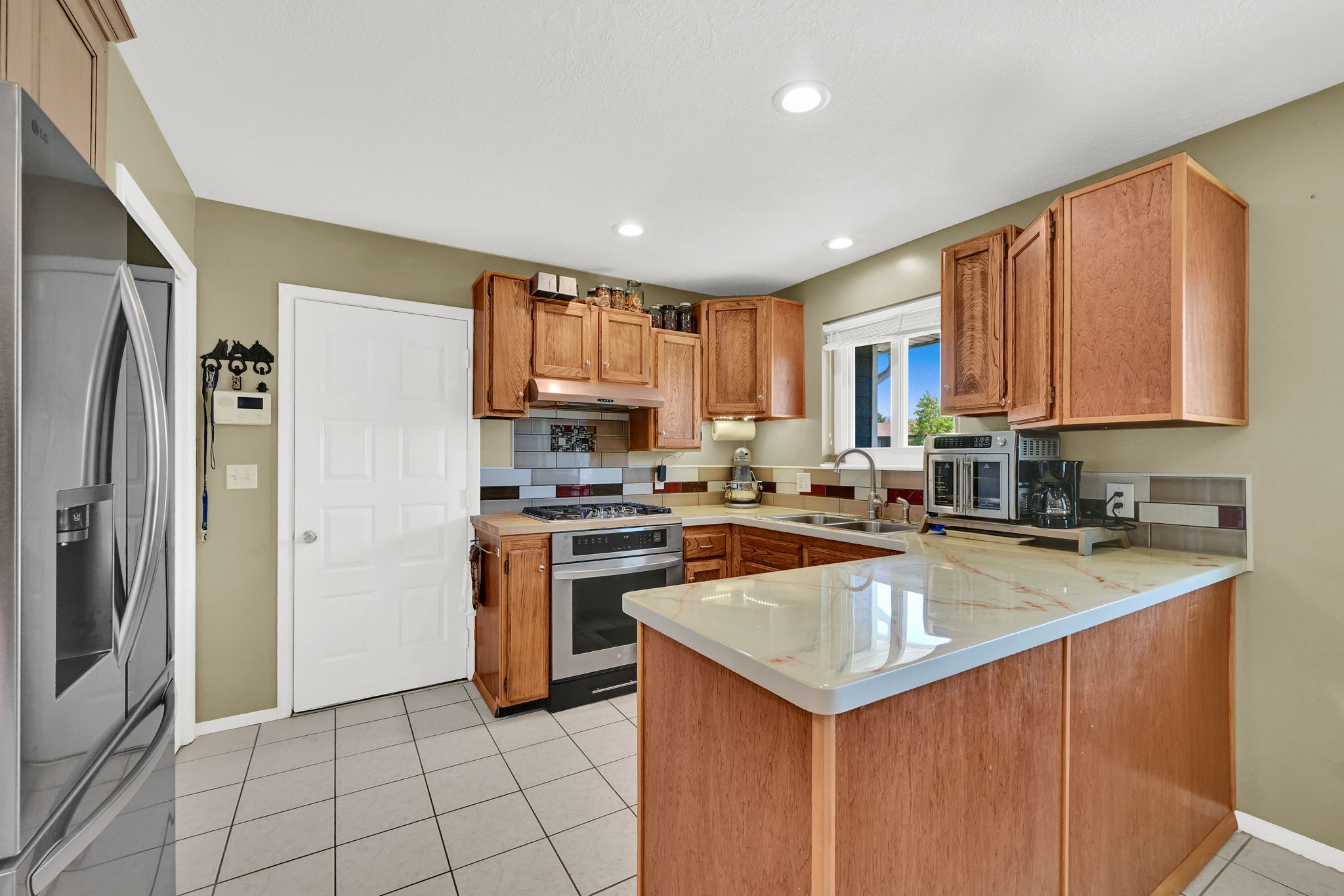 Kitchen featuring light wood cabinetry, a light-toned countertop, stainless steel appliances, and a tiled backsplash