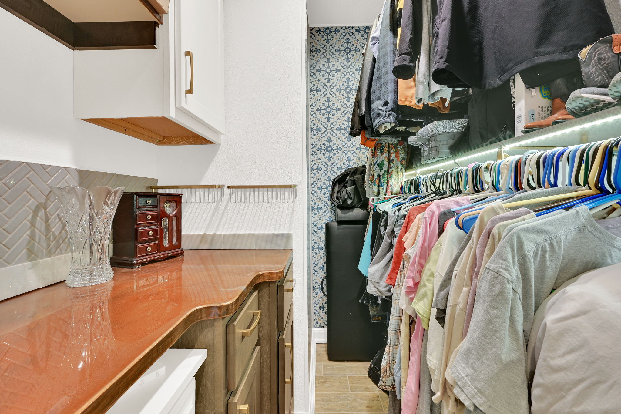 Custom closet organization system featuring patterned wallcovering, integrated lighting, and tile flooring