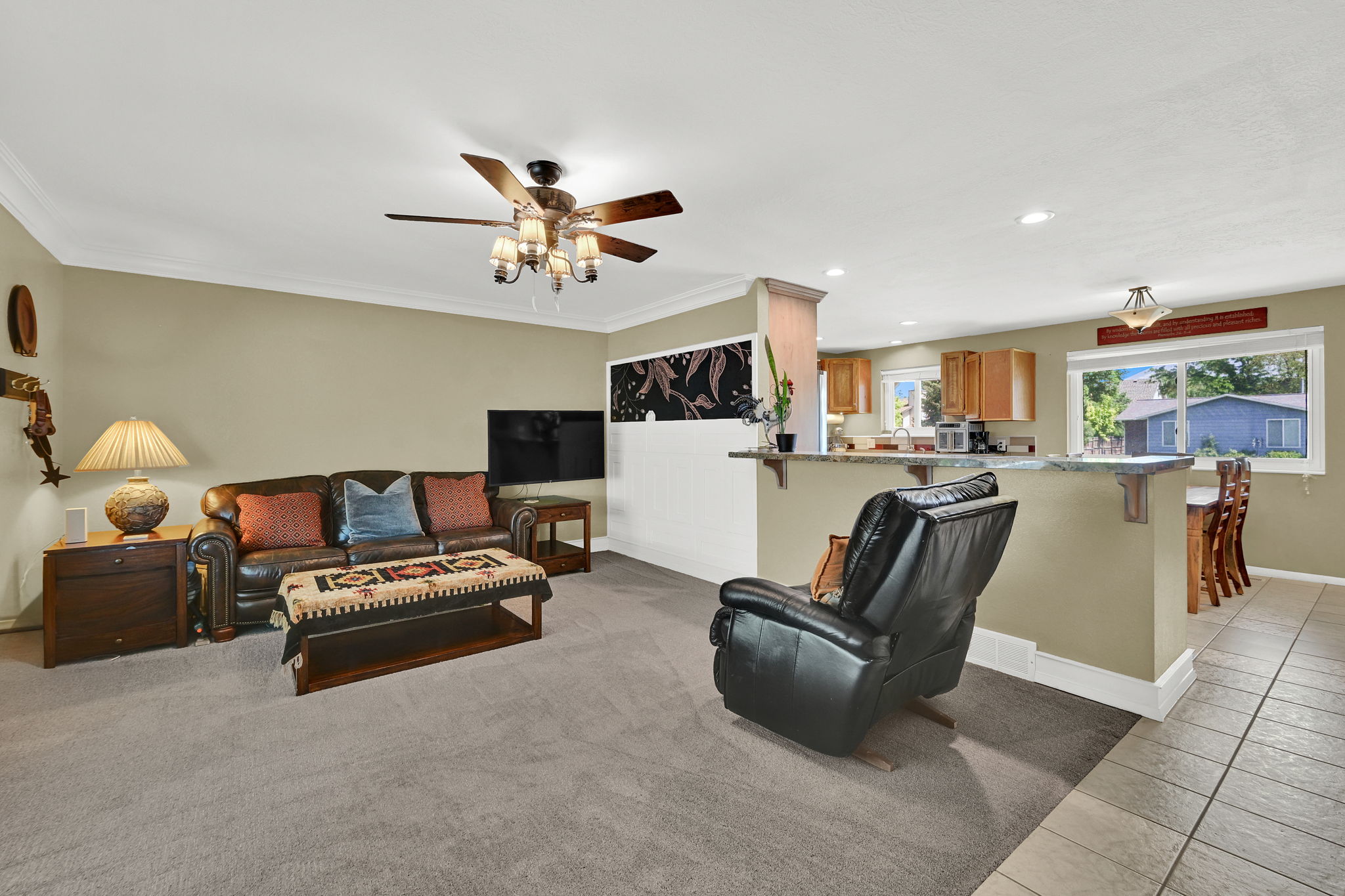 Open-concept living area featuring a ceiling fan with integrated lighting, crown molding, and neutral wall tones