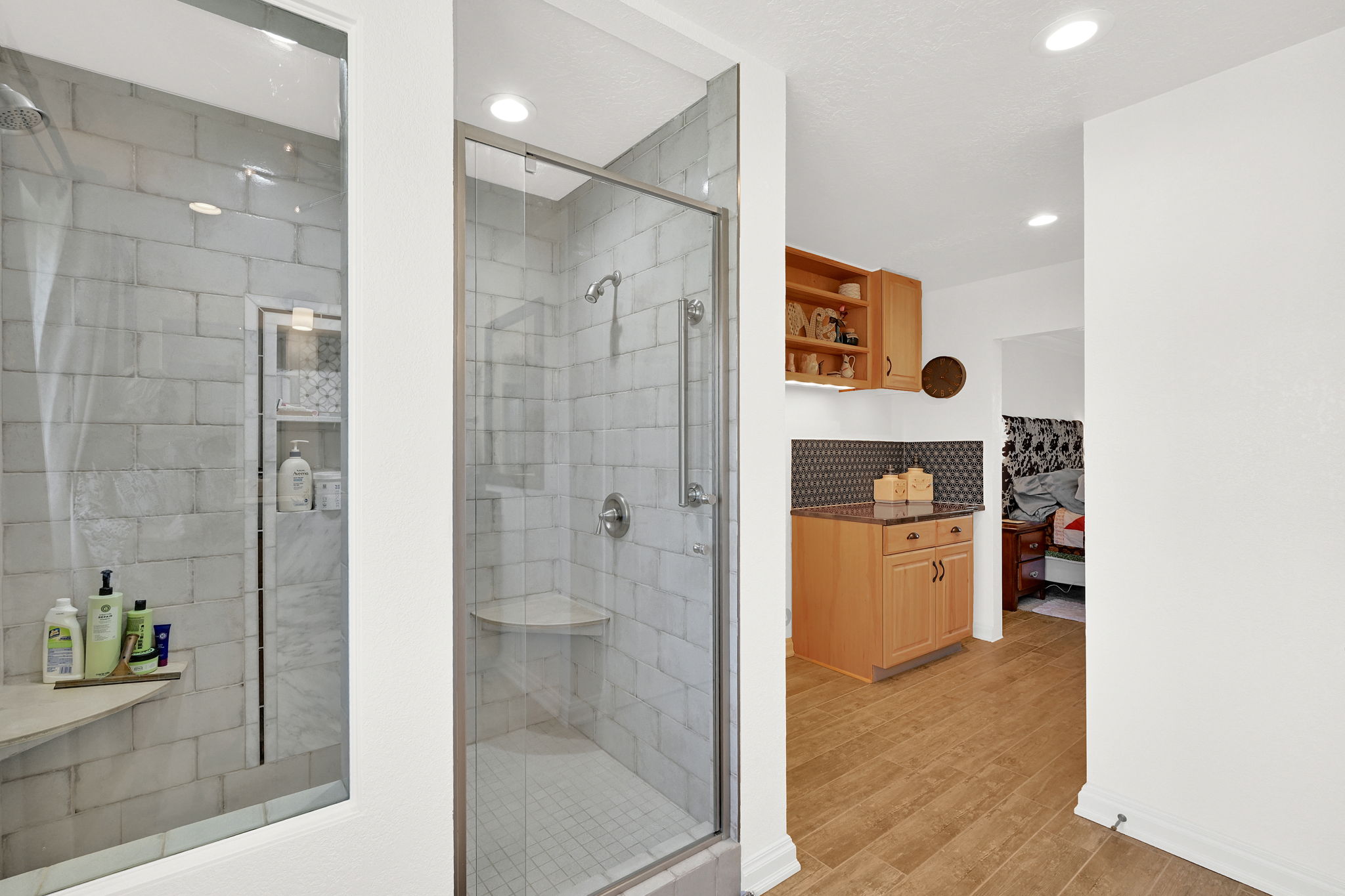 Walk-in shower with clear glass enclosure, subway tile surround, built-in shelving, and a corner bench