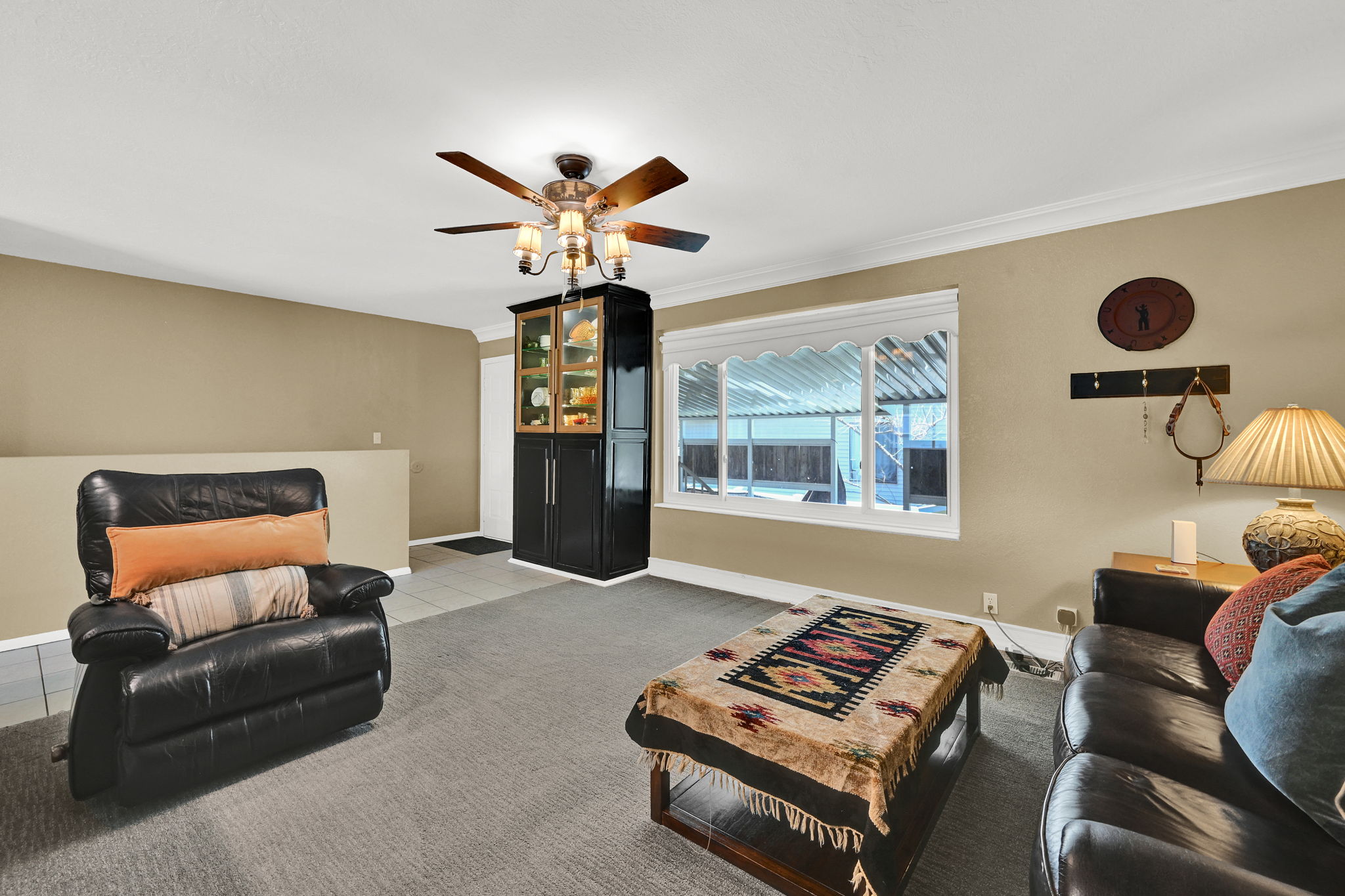 Living area featuring a ceiling fan with integrated lighting, a large window with white trim, and light beige wall paint