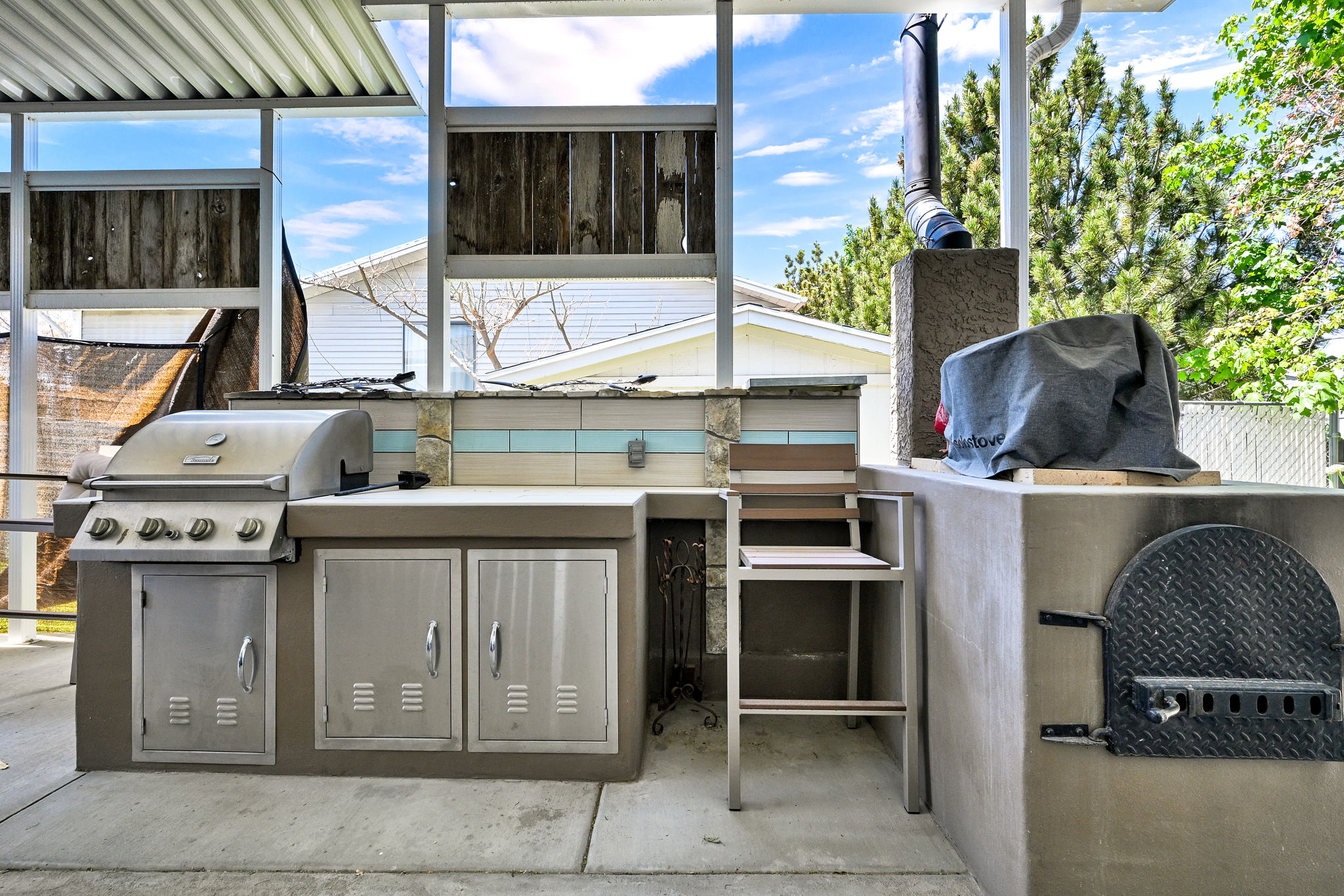 Outdoor kitchen featuring a built-in grill, multiple stainless steel storage cabinets, concrete countertops, and a concrete-clad pizza oven with a metal door