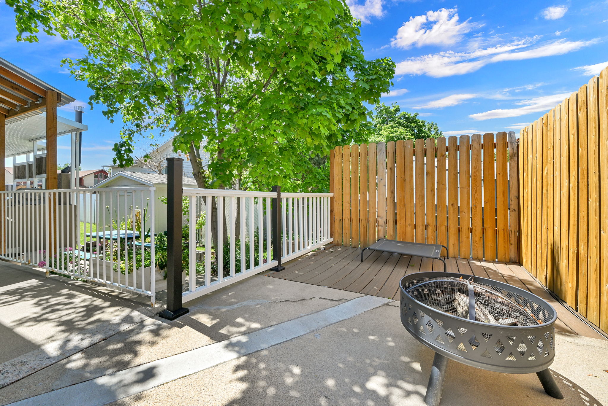 Outdoor patio space featuring a metal fire pit, wood-finish decking, and a privacy fence