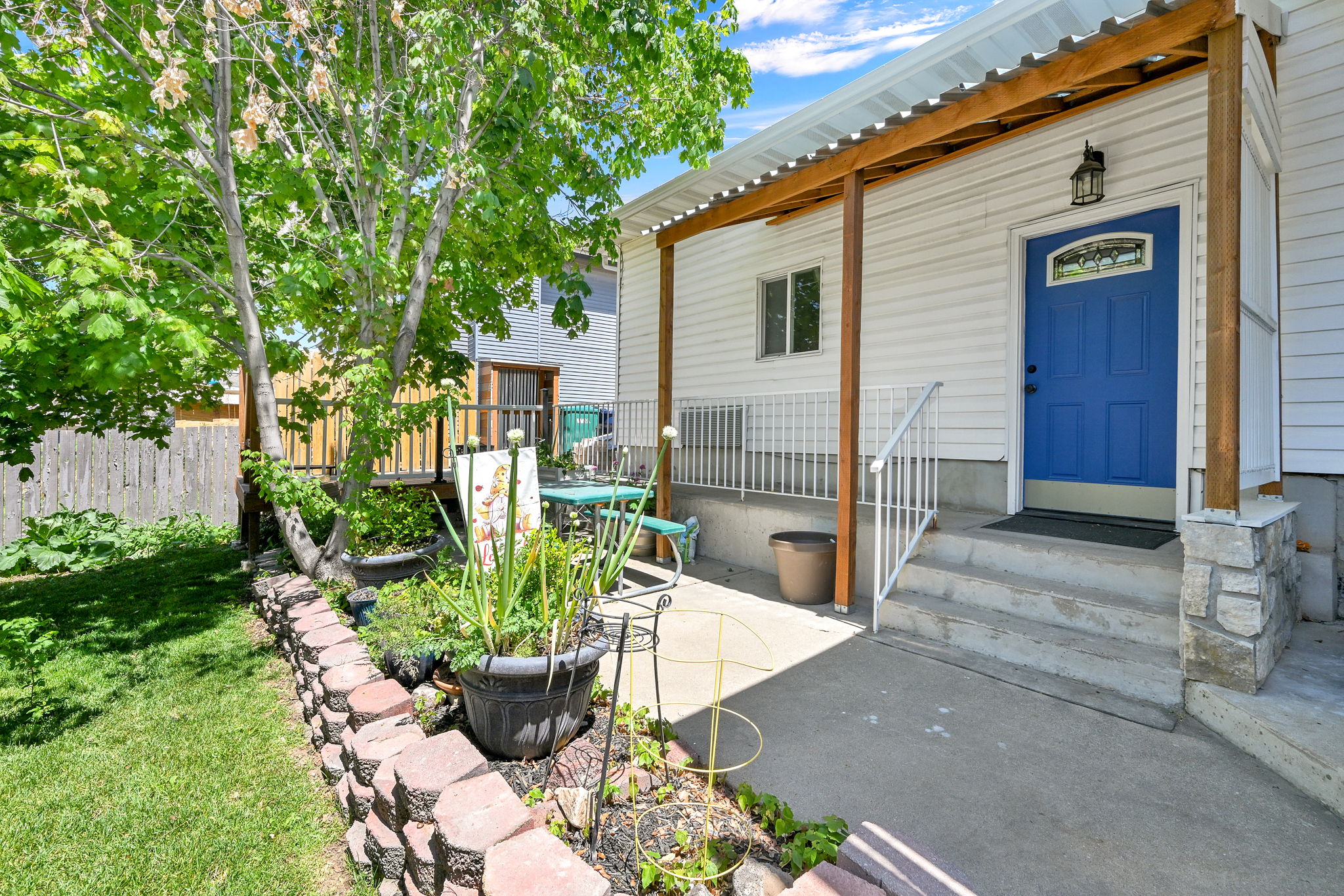 Covered concrete porch with stone-clad pillar, white siding, and a vibrant blue entry door