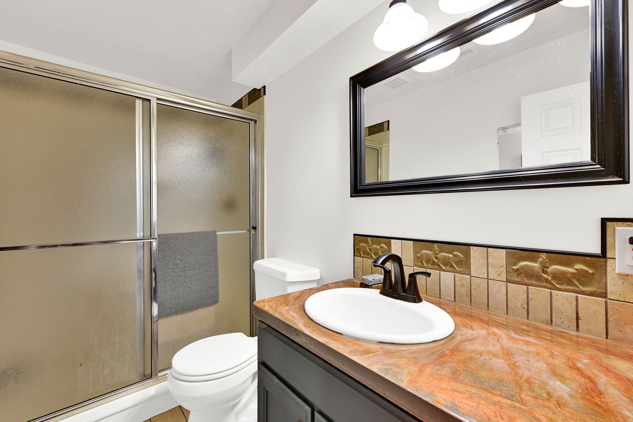 Bathroom featuring a full vanity with an oval sink, dark cabinet, and a richly veined countertop