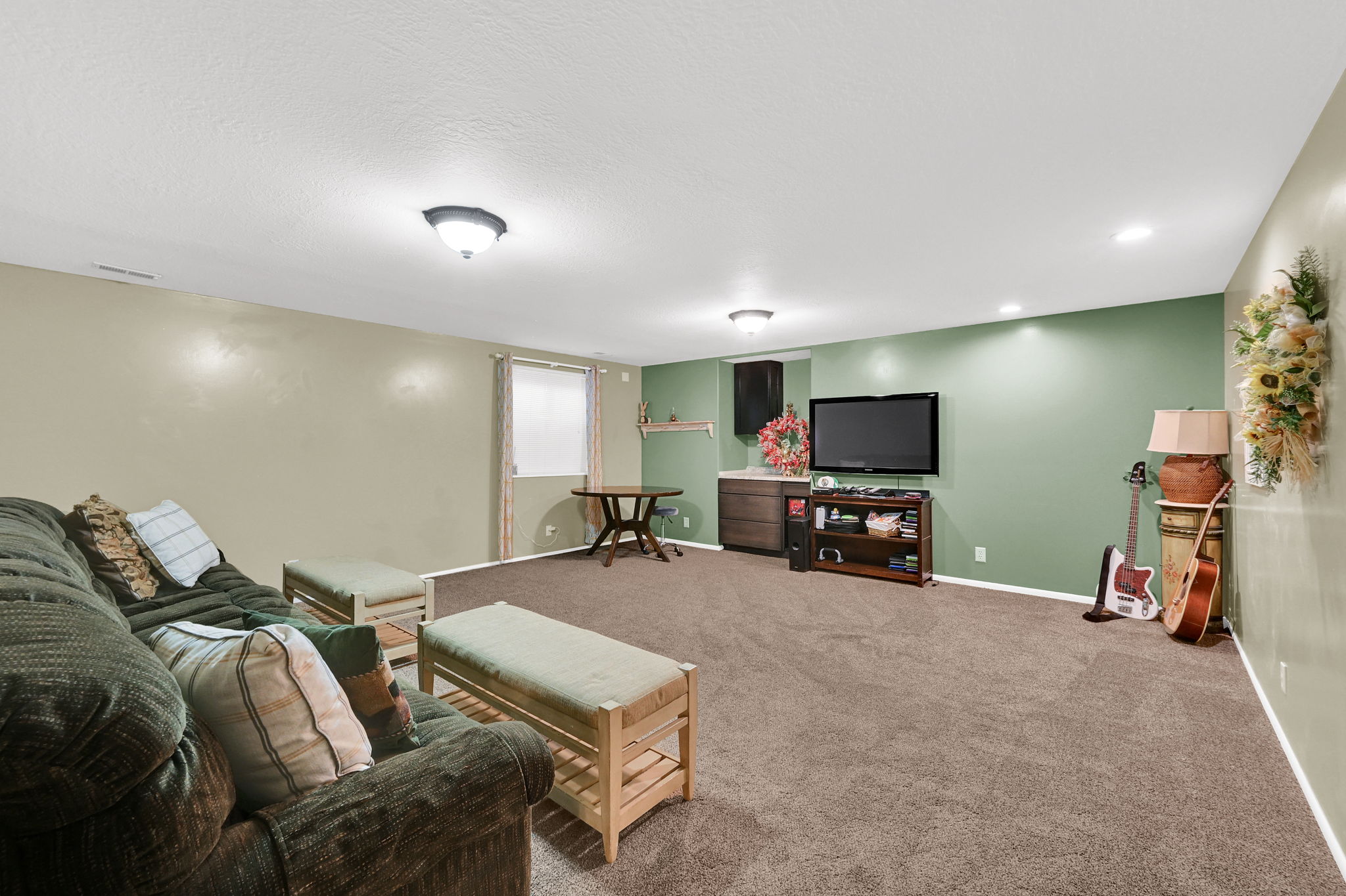 Spacious room featuring carpeting, recessed lighting, a built-in countertop with dark wood-finish cabinetry, a window with a roller shade, and a round wooden table