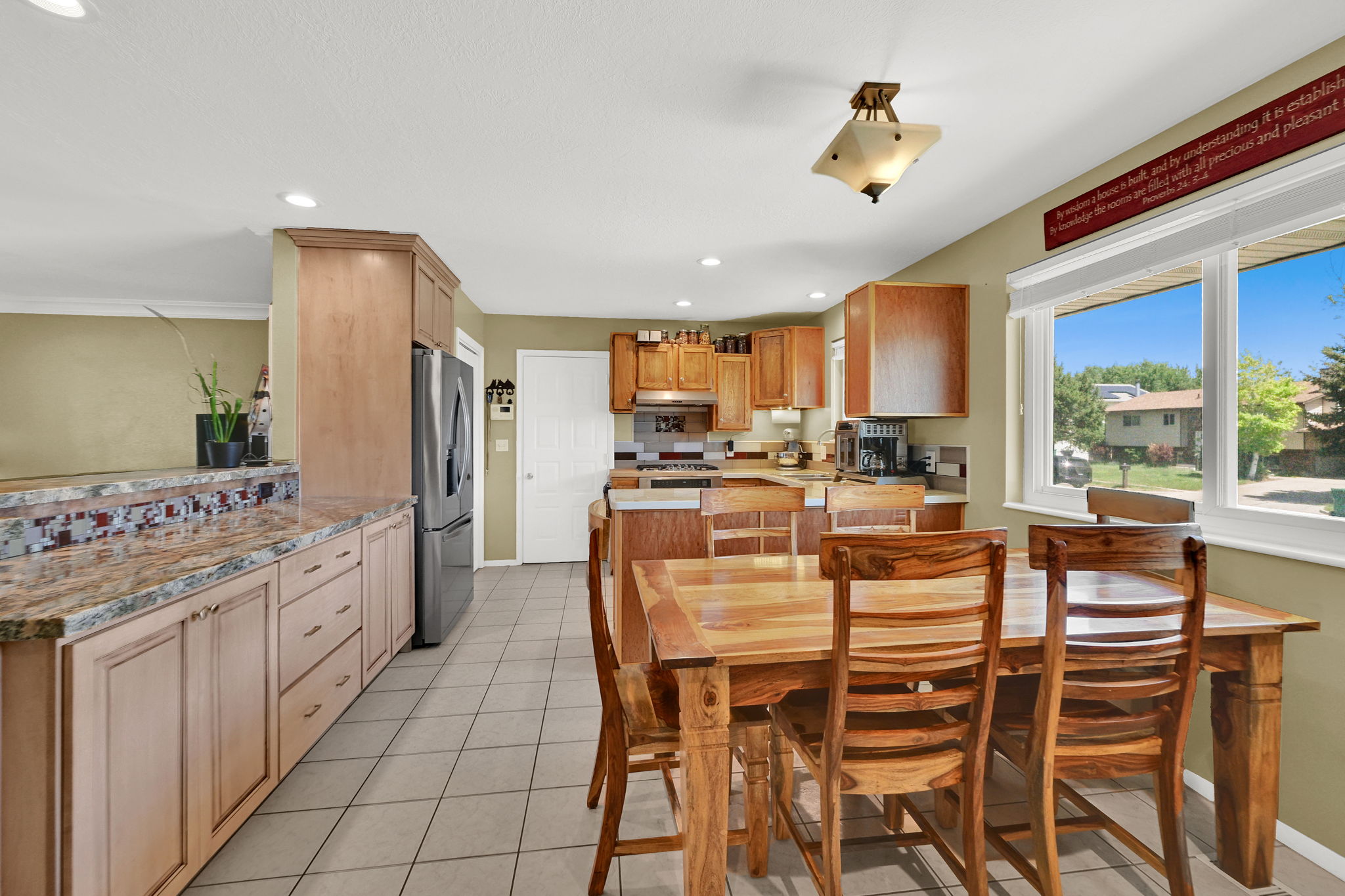 Kitchen and dining area featuring light wood cabinetry, stone countertops, stainless steel appliances, and tile flooring