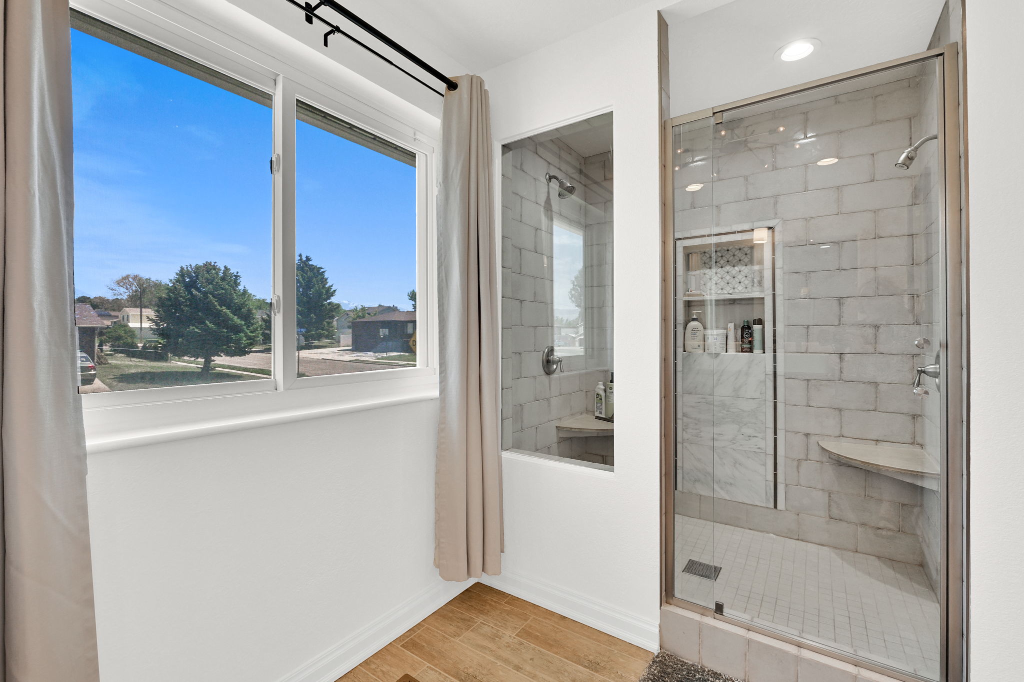Glass-enclosed shower featuring subway tile surround, built-in shelving, a corner bench, and a rainfall showerhead