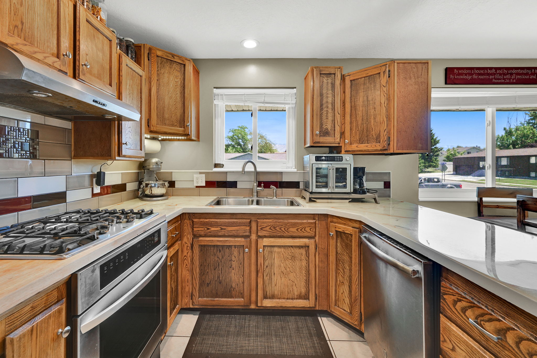 U-shaped kitchen featuring wood cabinetry, stainless steel appliances, a gas range with range hood, double basin sink, and tile backsplash