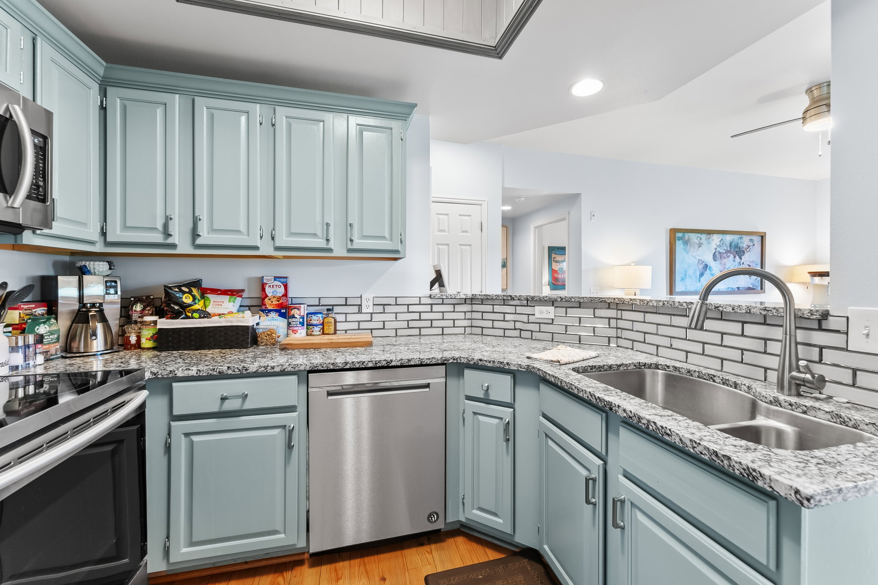Kitchen featuring light blue cabinetry, stainless steel appliances, a double basin sink with gooseneck faucet, light-toned granite countertops, and a subway tile backsplash