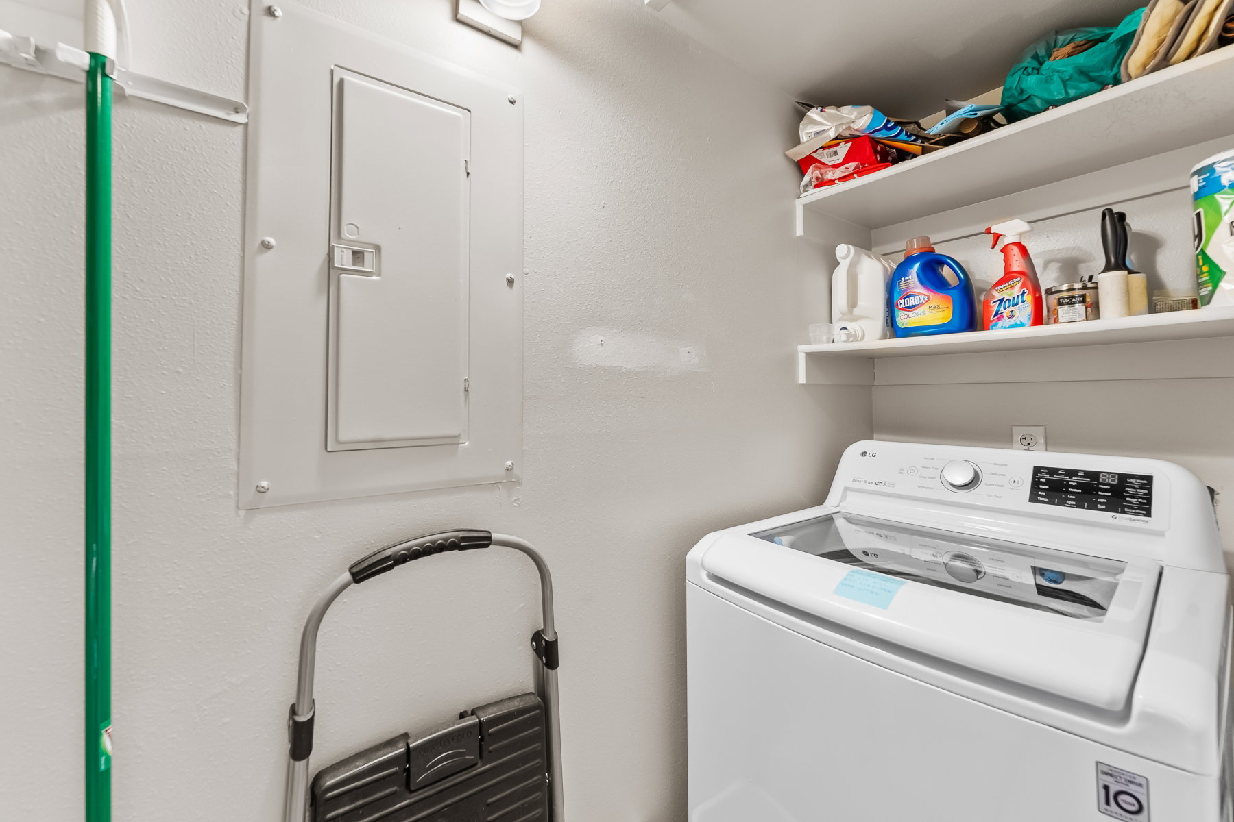 Dedicated laundry space featuring a built-in top-load washing machine and white floating shelves for storage