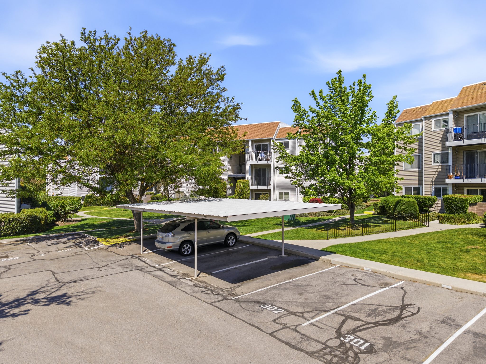Designated carport parking space with a protective metal roof, surrounded by mature trees and manicured green spaces
