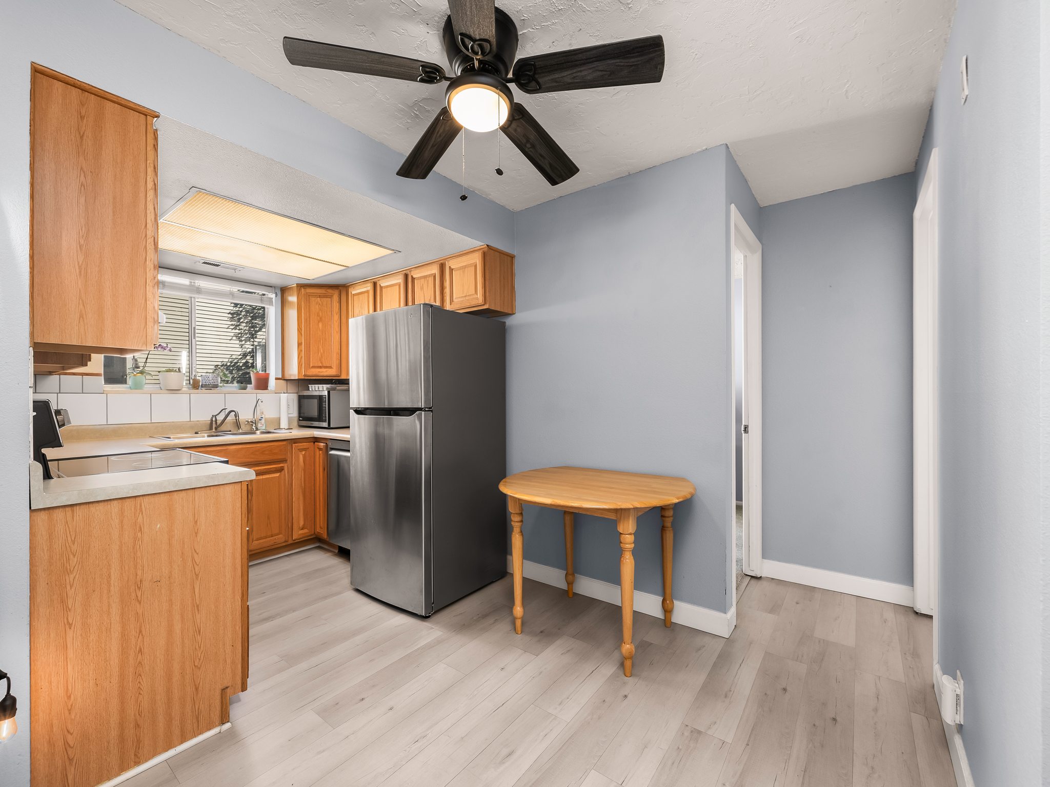 Kitchen featuring light wood-finish cabinetry, a stainless steel refrigerator, white subway tile backsplash, and light wood-finish flooring