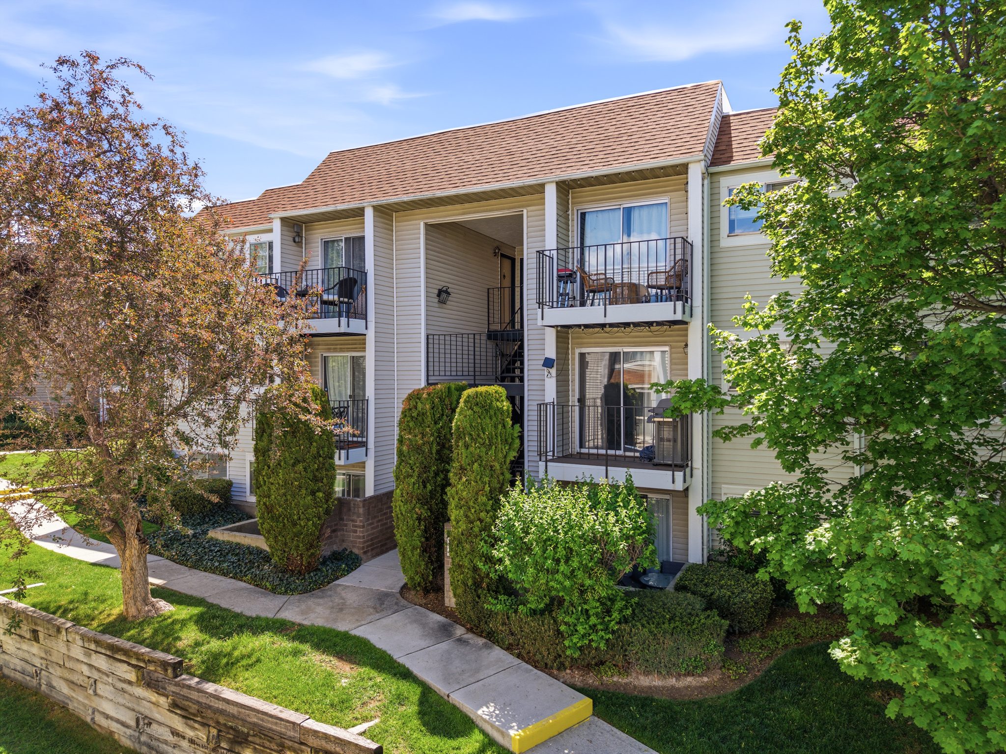 Multi-level building with individual balconies, light-colored siding, and a brown shingled roof