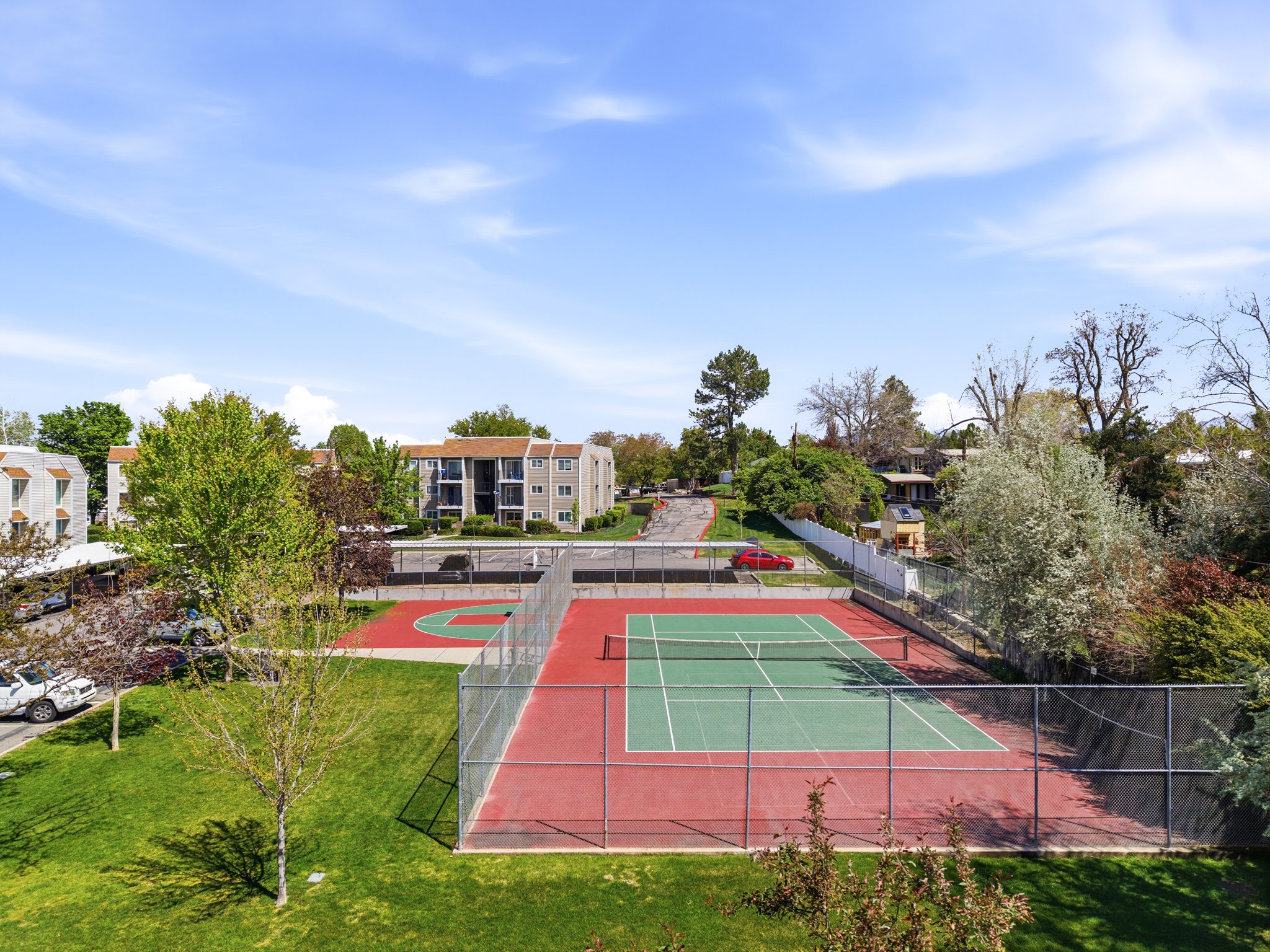 Outdoor tennis court with green and red surface, surrounded by black chain-link fencing